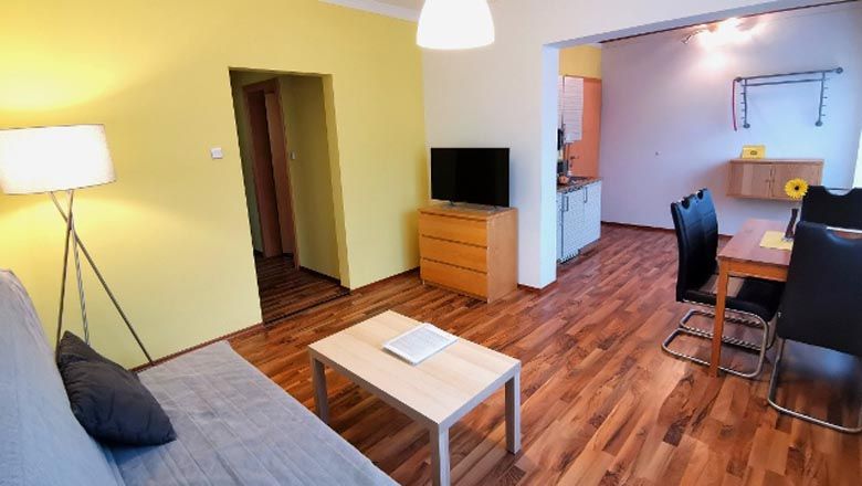 Moderná obývacia izba s drevenou podlahou, pohovkou, stolom, TV a jedálenským kútom.