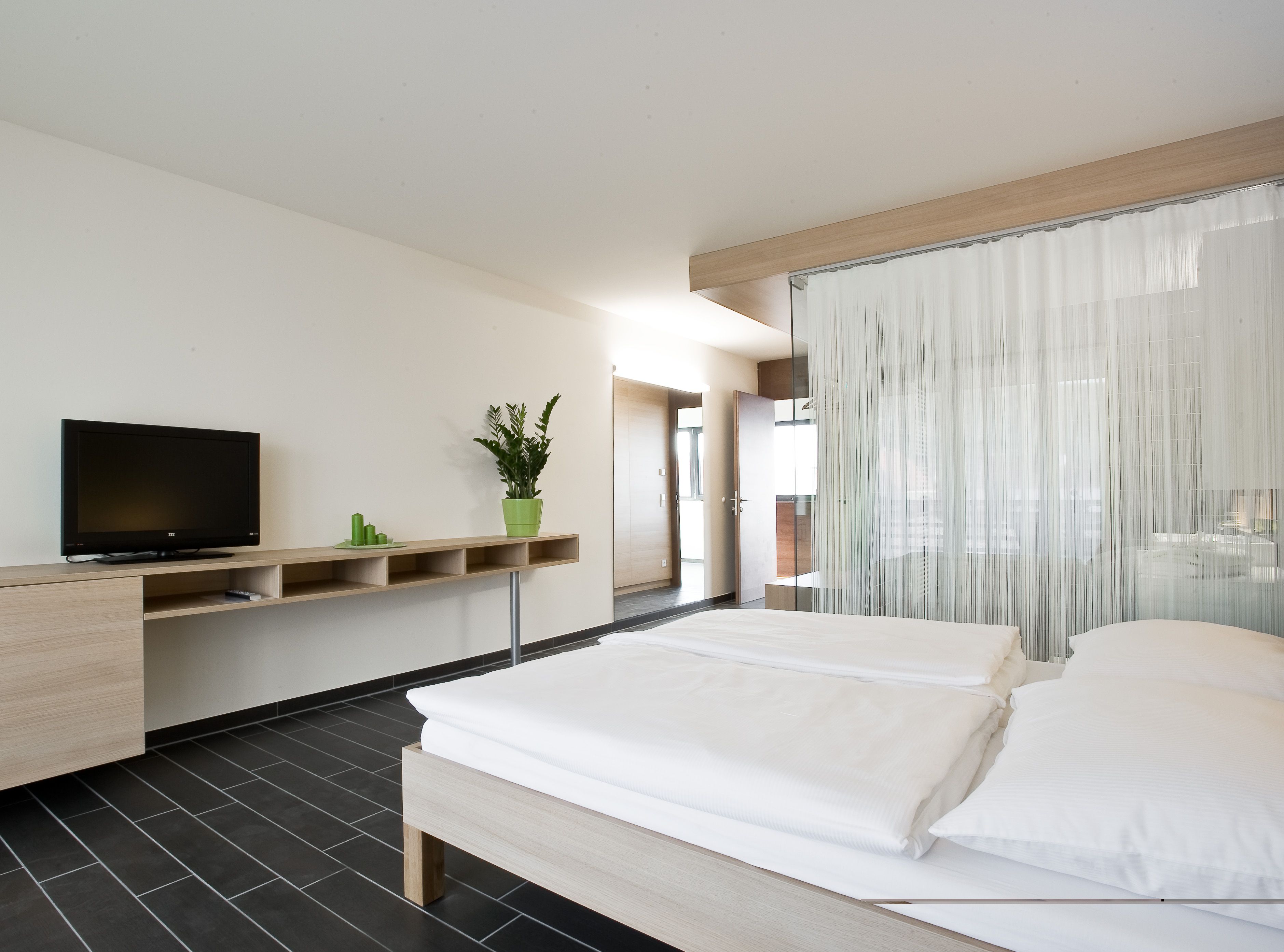 Moderná hotelová izba s manželskou posteľou, televízorom a rastlinami.