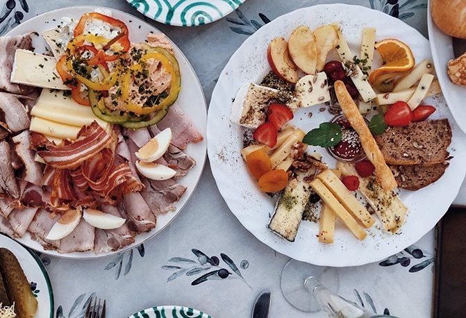 Dva taniere s údeninami, syrom, zeleninou a ovocím na stole.