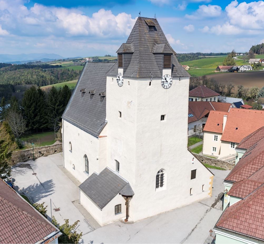 Opevnený kostol Lichtenegg s mohutnou vežou s hodinami a okolitými budovami.