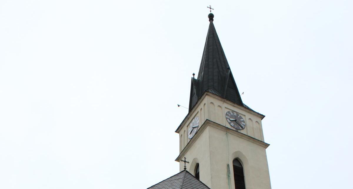Kostolná veža s hodinami a špicatou strechou pred jasnou oblohou.