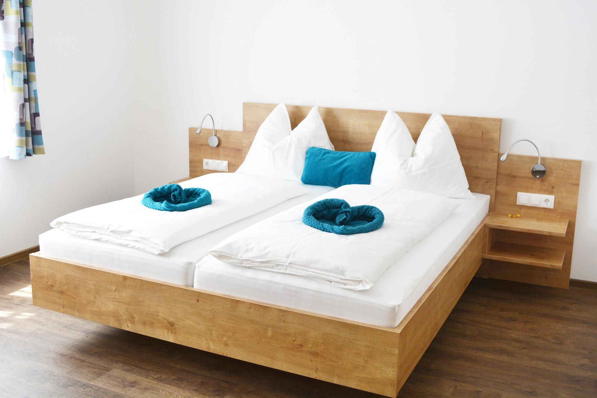 Moderná izba pre hostí s manželskou posteľou, bielymi perinami a modrými vankúšmi.