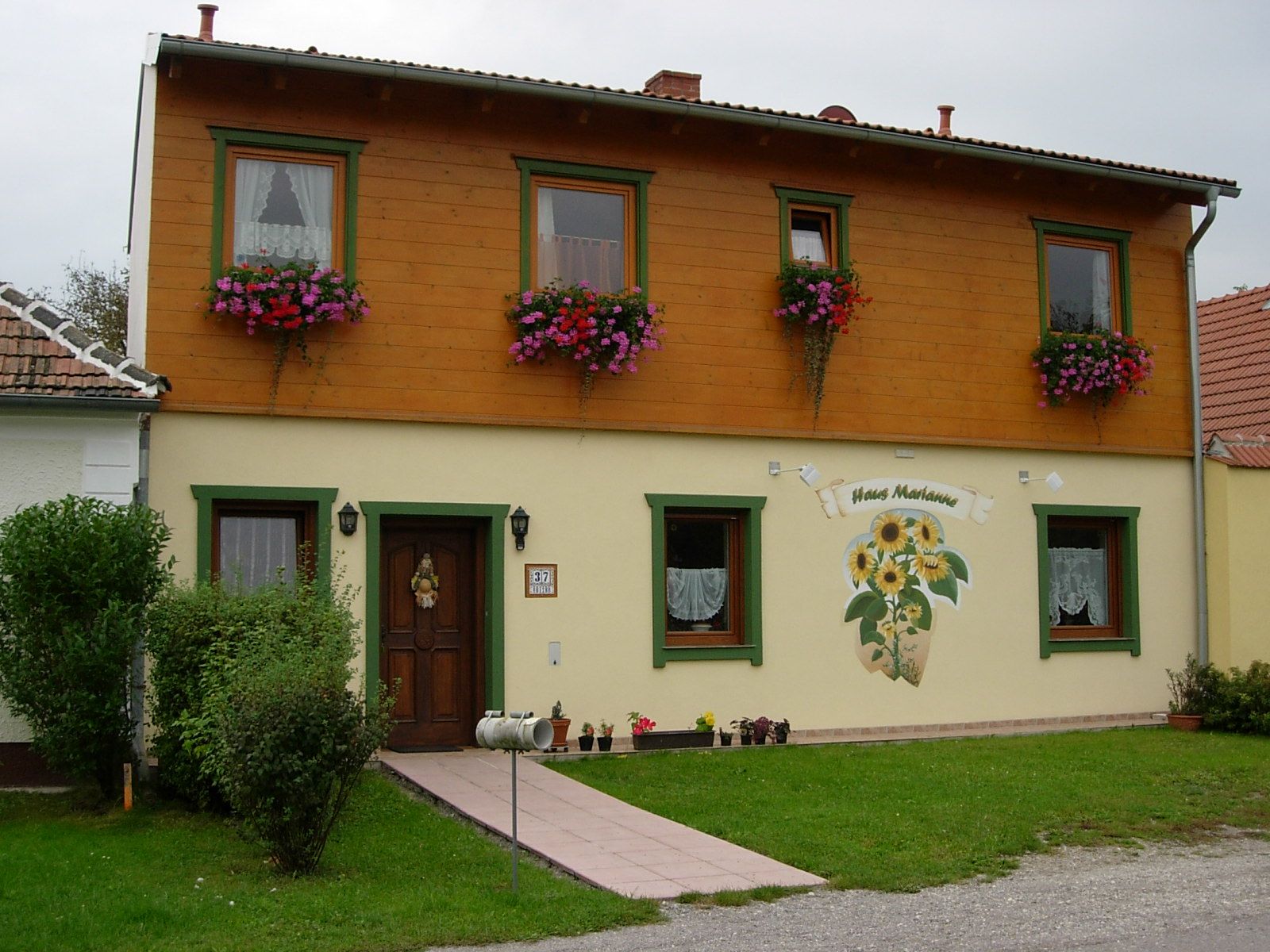 Dvojpodlažný dom s dreveným obložením a kvetinovými truhlíky s označením "Haus Marianne".