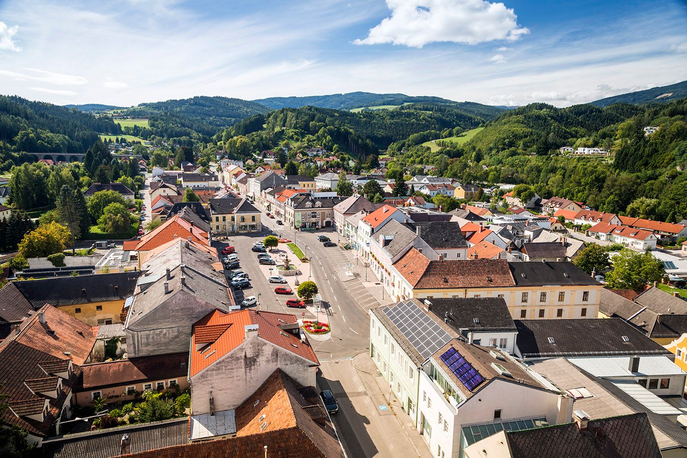 Letecký pohľad na námestie Aspang Markt s červenými strechami a zelenou krajinou v pozadí.