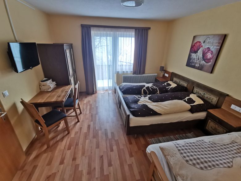 Útulná spálňa s manželskou posteľou, stolom, stoličkami a prístupom na balkón.