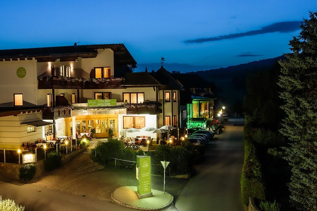 Vonkajší pohľad na hotel Vitalzeit Weber v noci, osvetlený teplým svetlom, obklopený stromami a zaparkovanými autami.