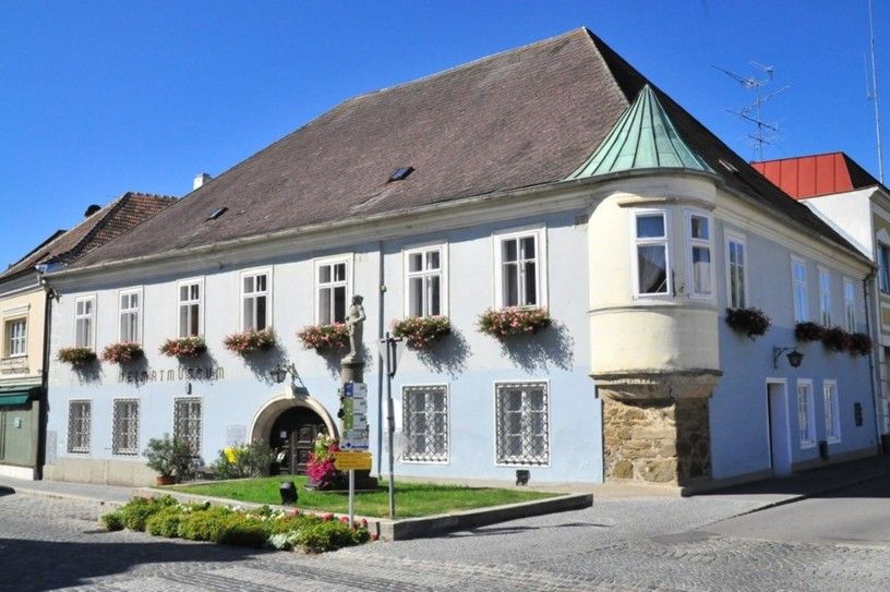 Historická budova s modrou fasádou a kvetinovými truhlíky, Múzeum miestnej histórie Langenlois.