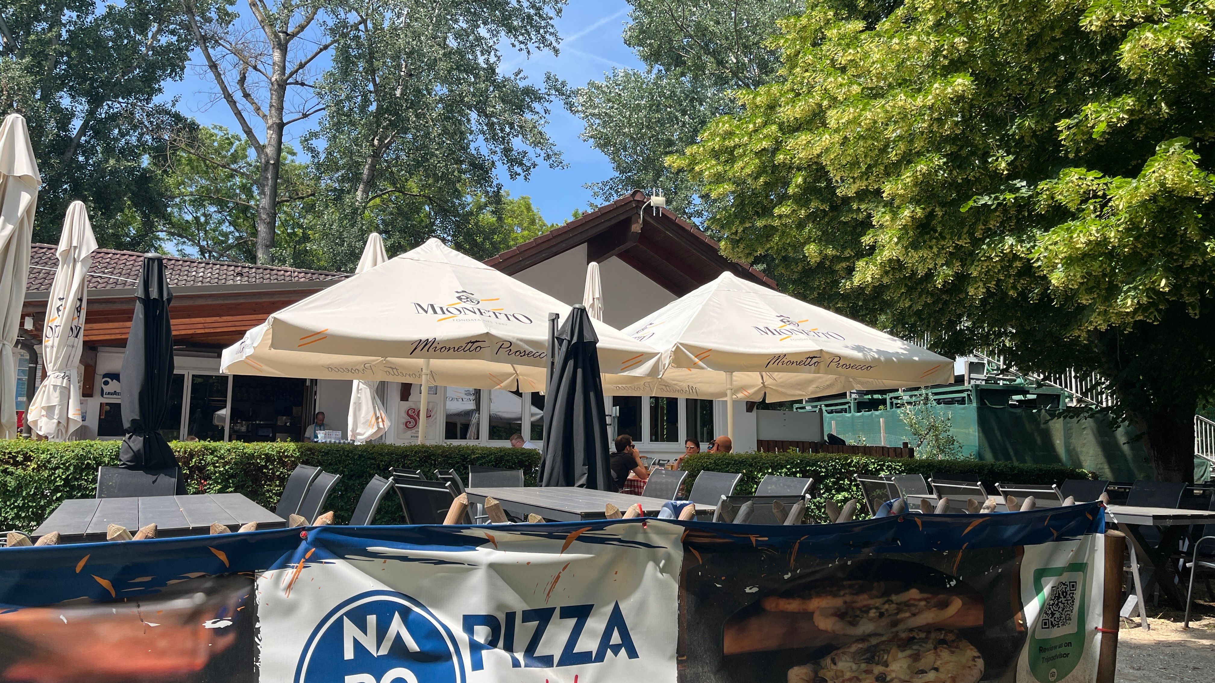 Záhrada pre hostí s výhľadom na budovu pizzerie, stromy v pozadí.