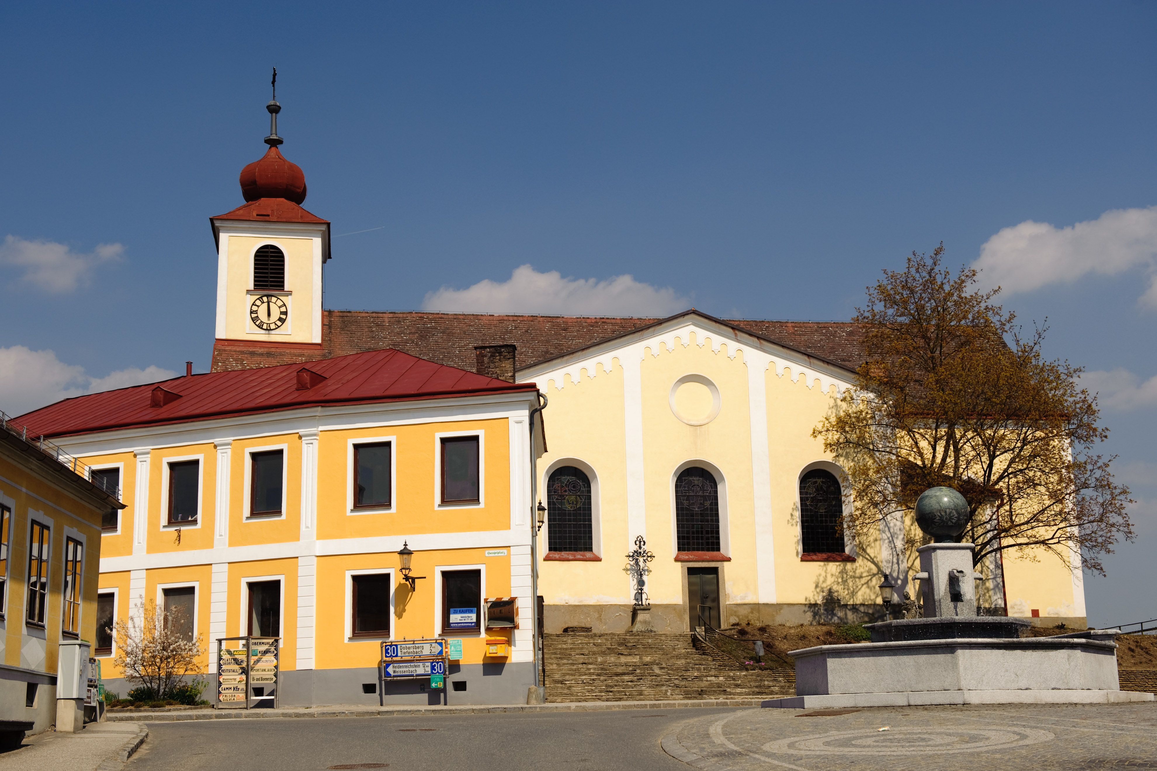 Kostol so žltou fasádou a vežou s červenou strechou na hlavnom námestí.