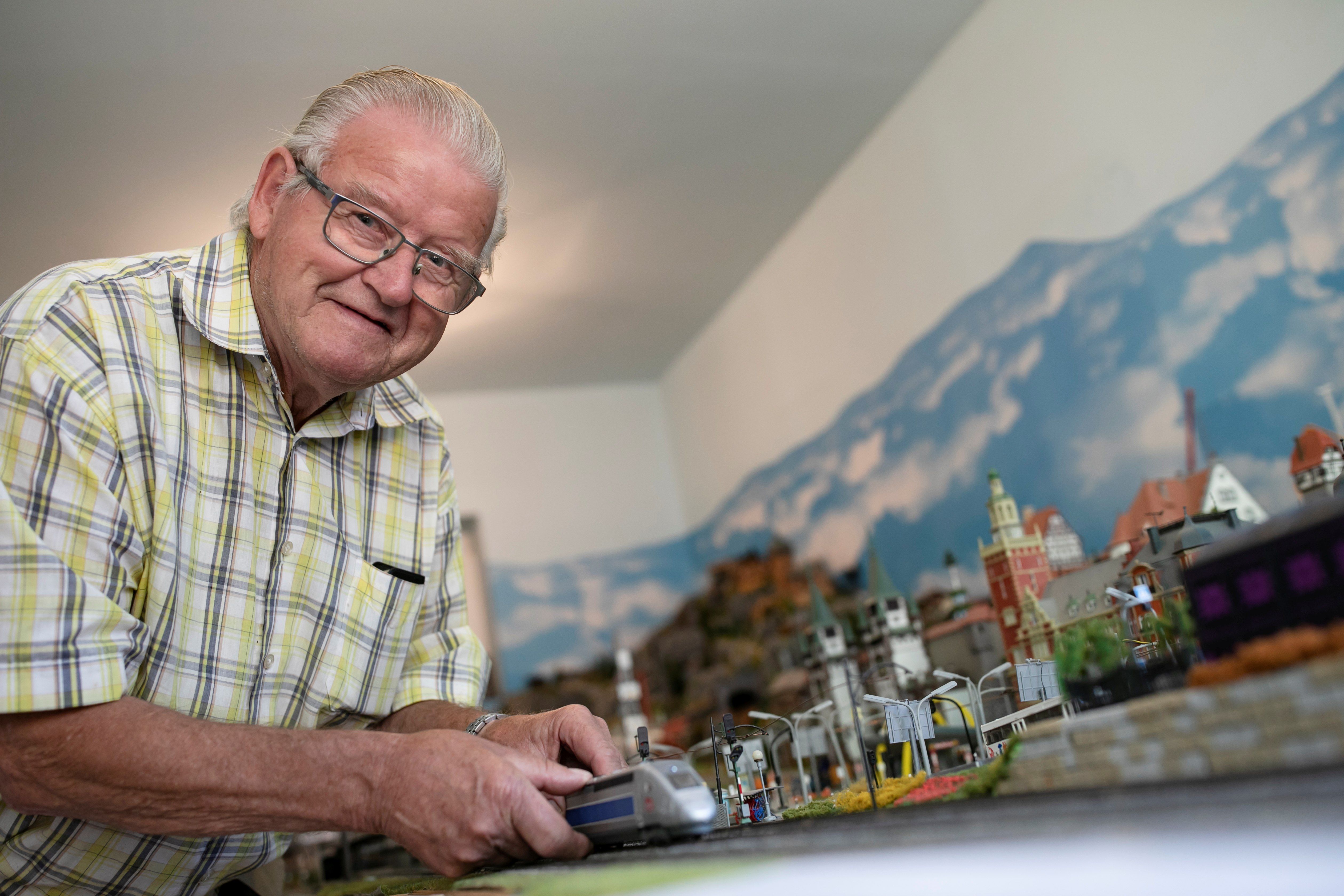 Dedo Moser stojí pred svojím modelovým železničným svetom a ukazuje lokomotívu. 