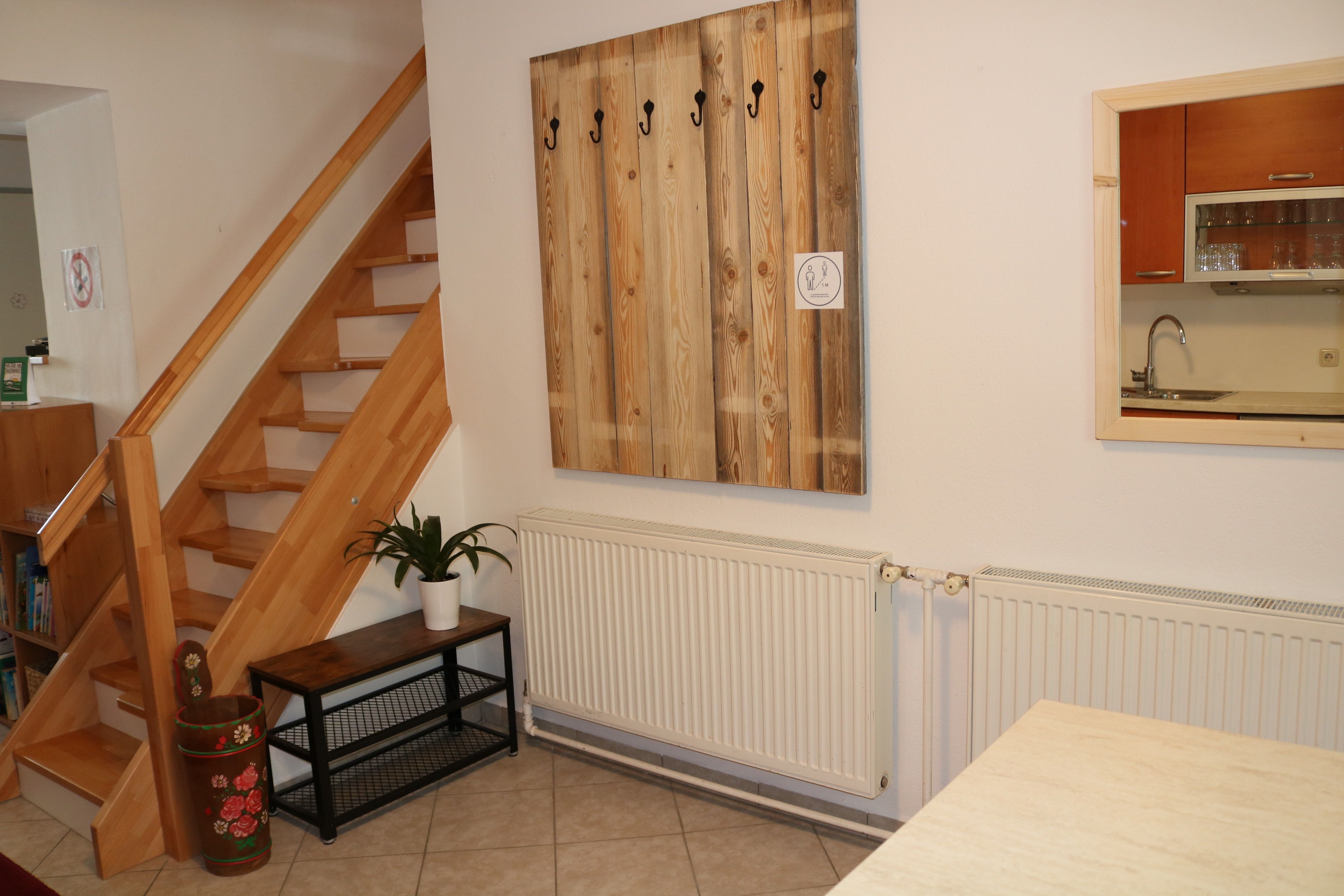 Interiér s dreveným schodiskom, šatníkom, rastlinou a kuchynským oknom.