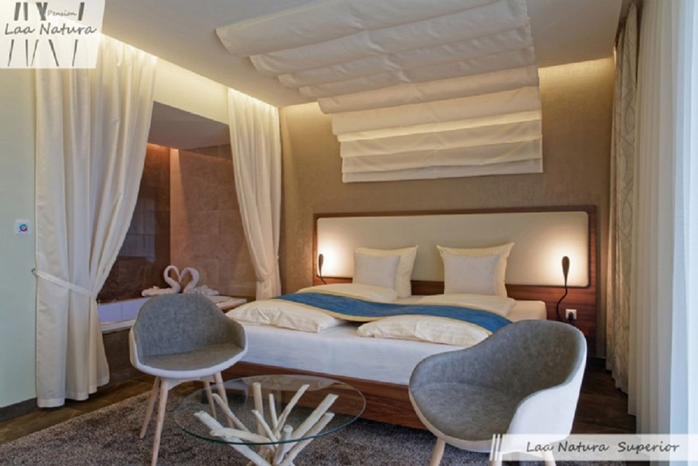 Moderná dvojlôžková izba s veľkou posteľou, dvoma sivými stoličkami a skleneným stolom.