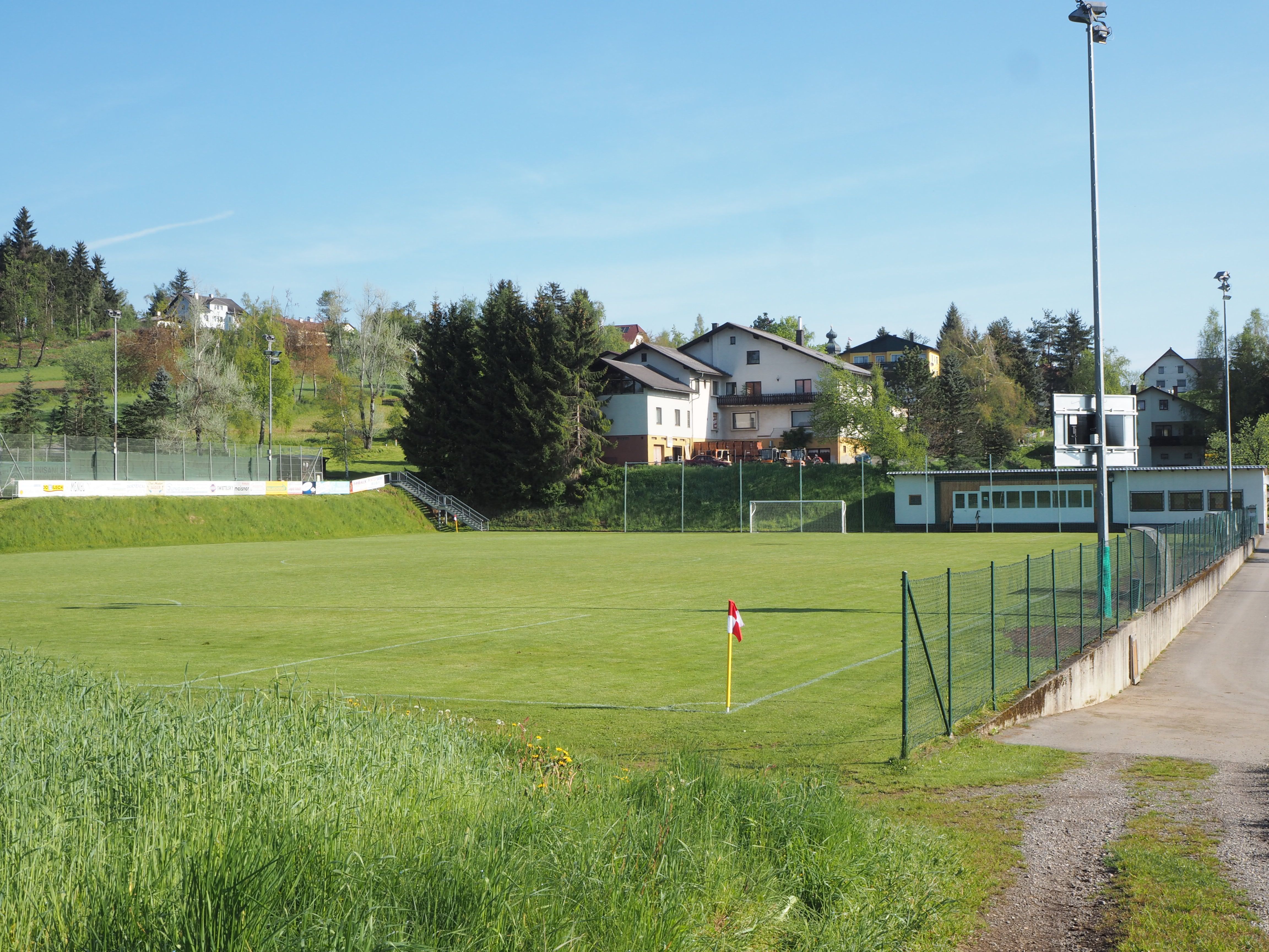 Prázdne futbalové ihrisko s okolitými budovami a stromami počas slnečného dňa.