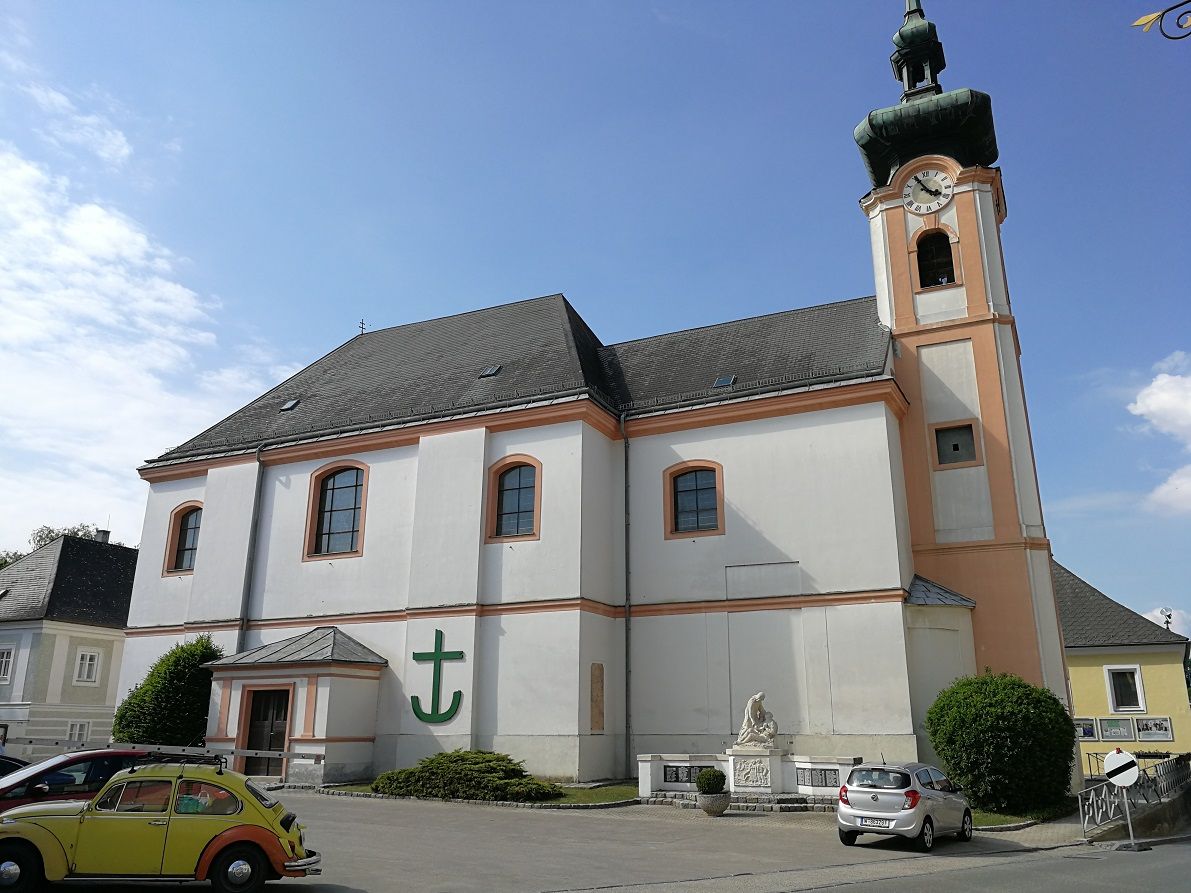 Farský kostol Würmla s hodinovou vežou a zaparkovanými autami.