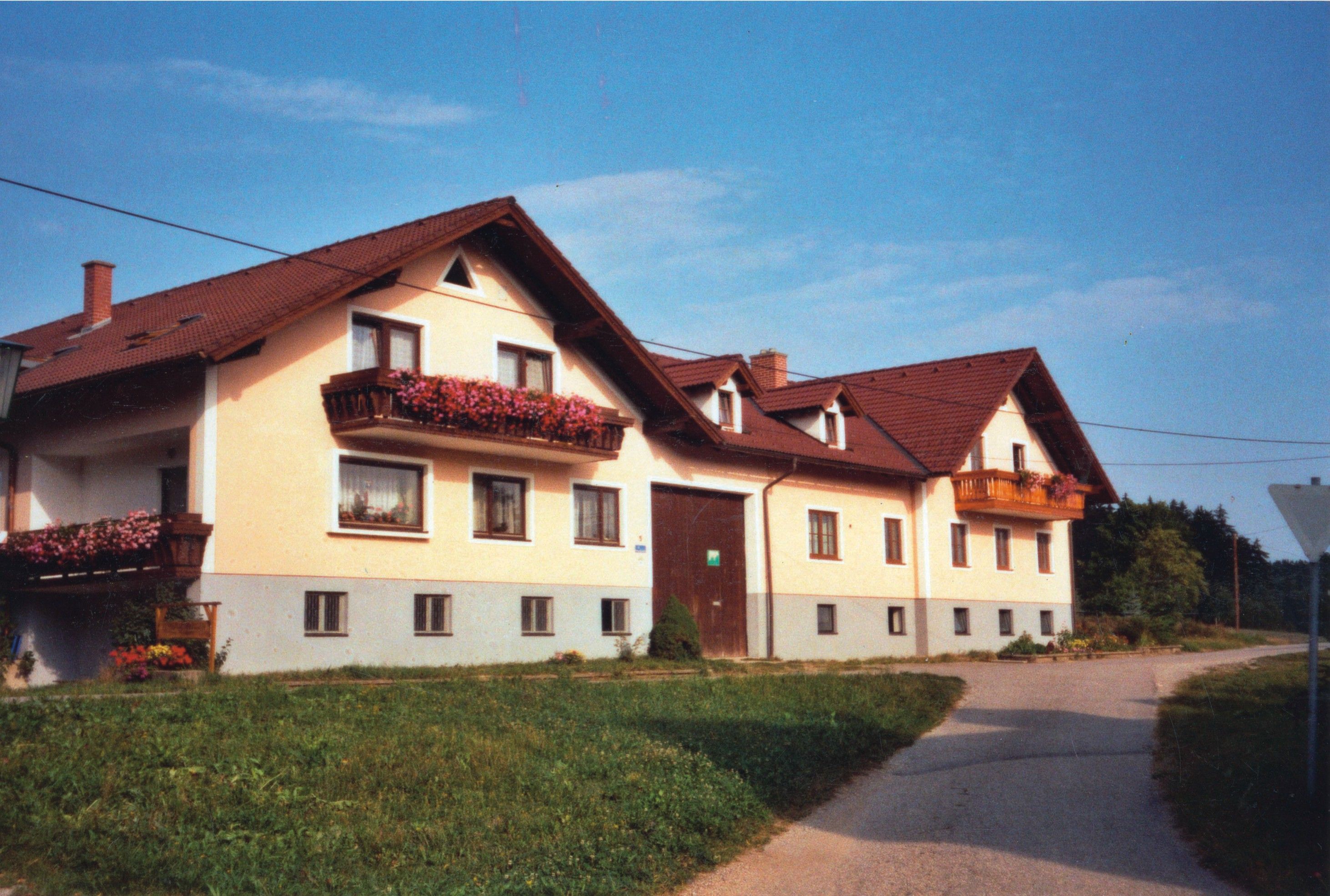 Veľký dvojpodlažný statok s červenými strechami a kvetinovými truhlíky na balkónoch.