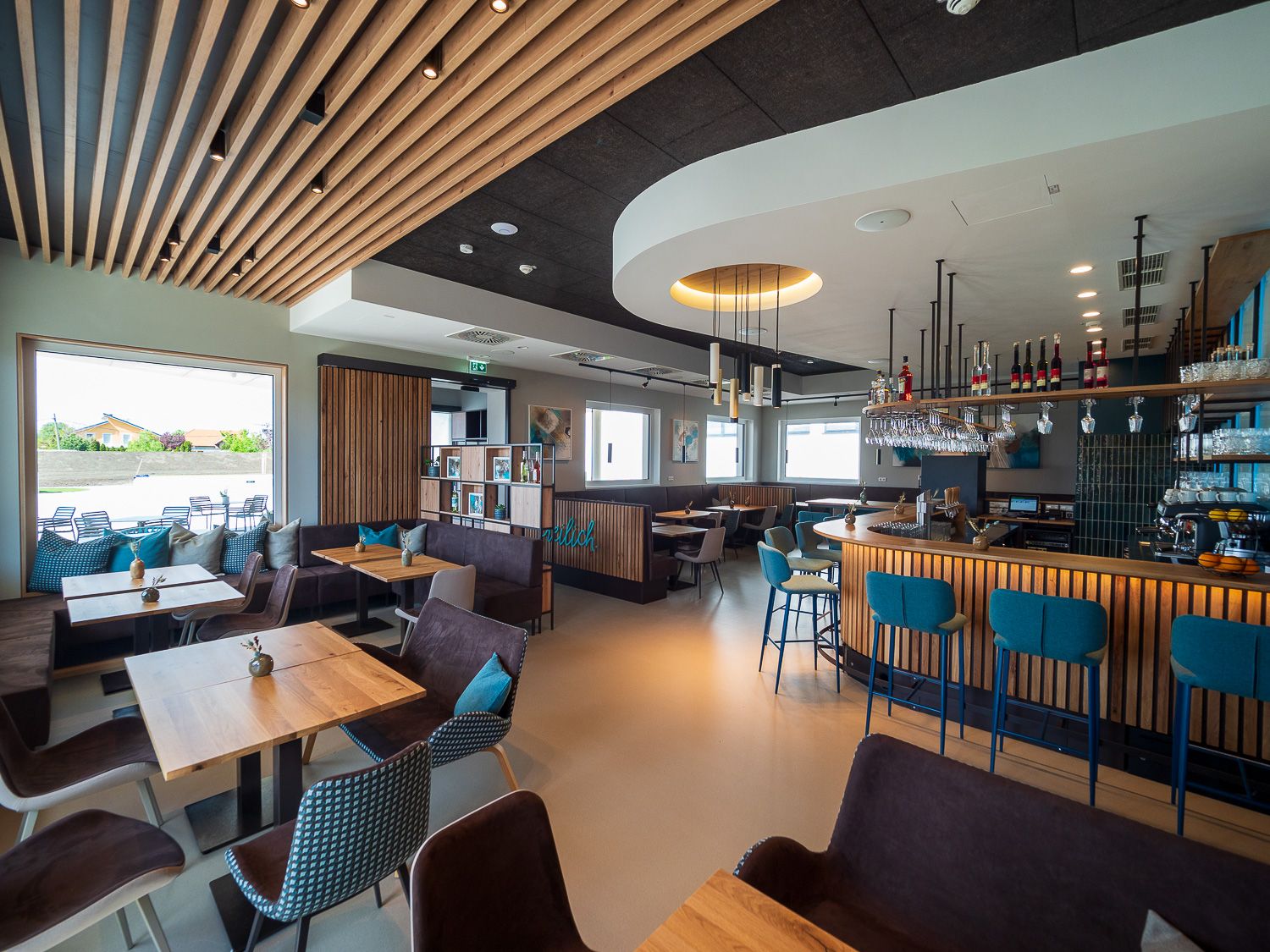 Moderné bistro s dreveným nábytkom, barom a veľkými oknami.