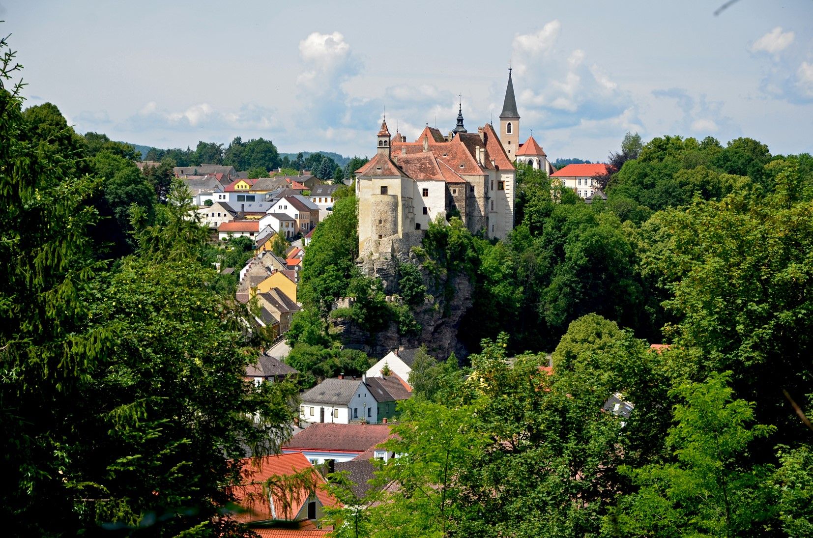 Pohľad na mesto Raabs s hradom na kopci, obklopené stromami a domami.
