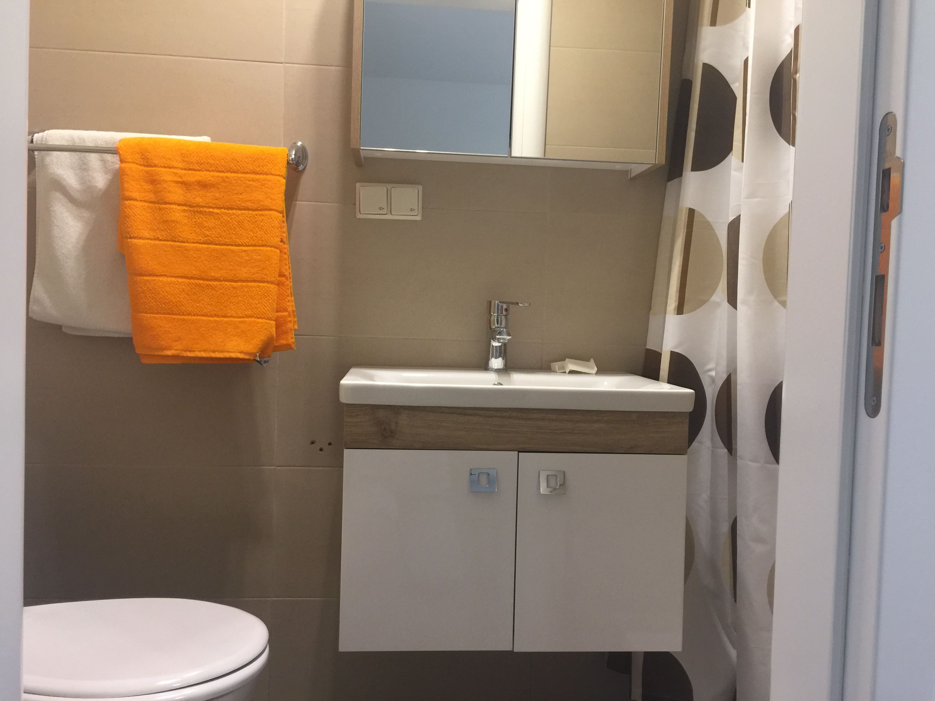 Malá kúpeľňa s umývadlom, zrkadlom, sprchovým závesom a uterákmi.