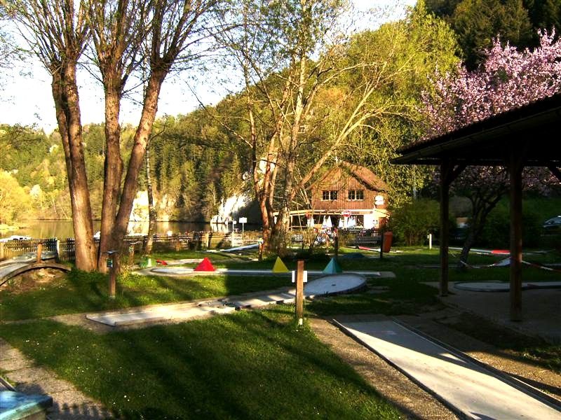 Minigolfové ihrisko so stromami a budovou v pozadí.