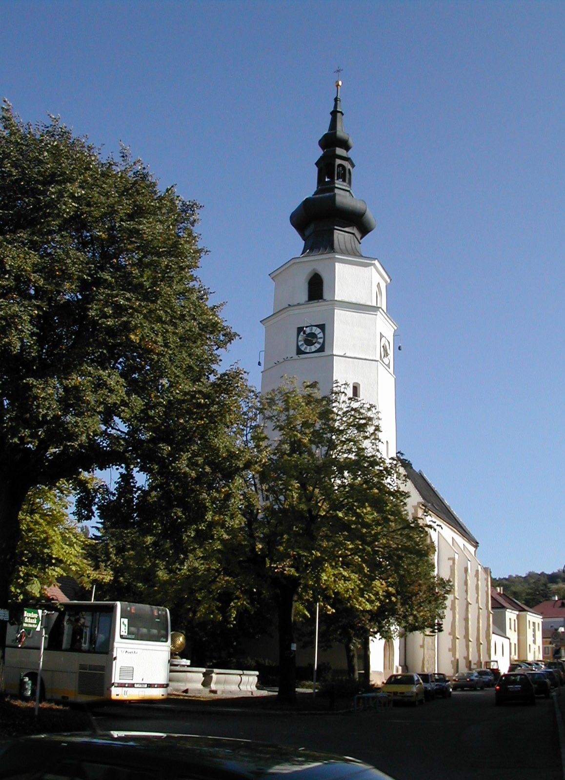 Farský kostol Königstetten s vežou a stromami v popredí.