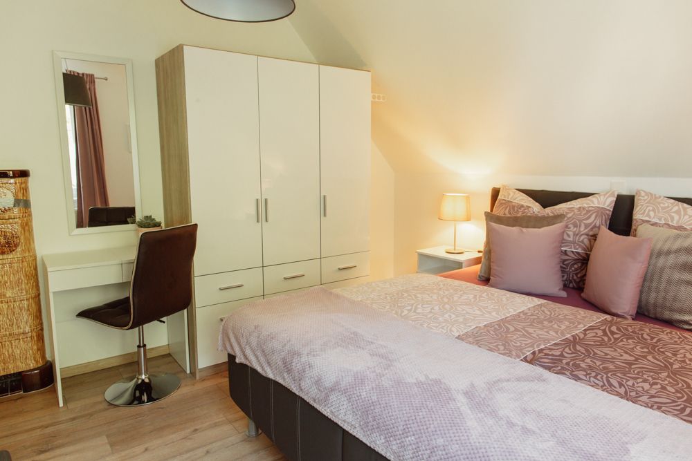 Spálňa s manželskou posteľou, šatníkovou skriňou, toaletným stolíkom a lampou.