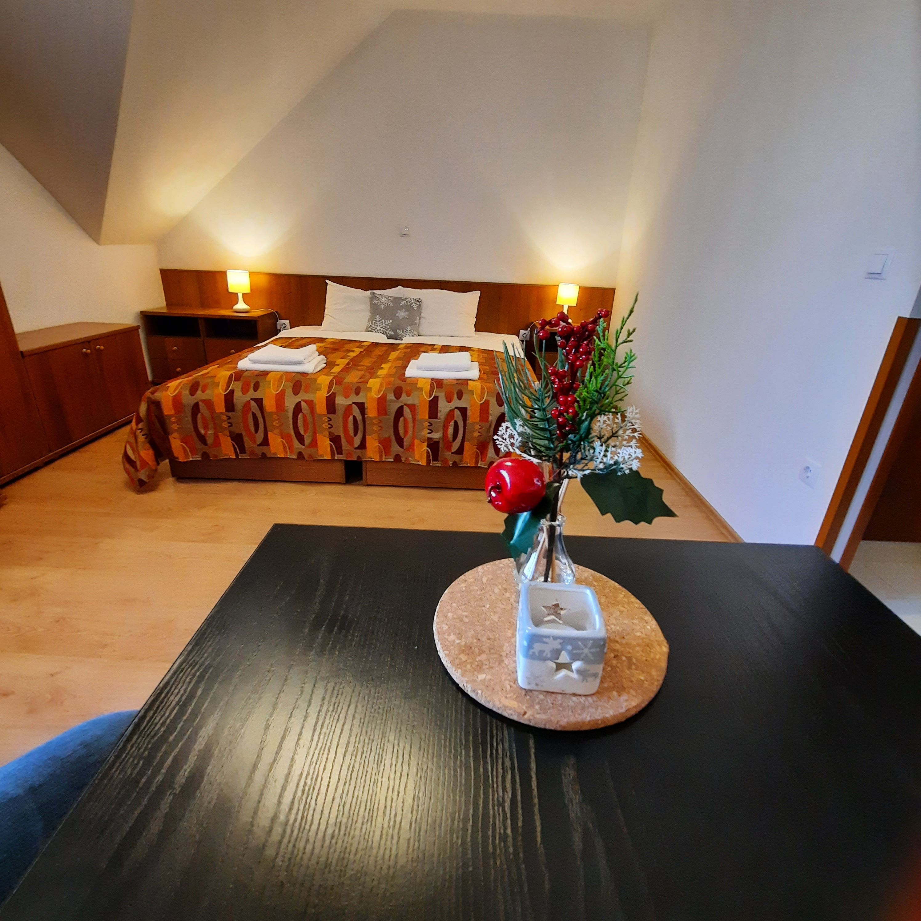 Útulná dvojlôžková izba s ozdobeným stolom v popredí a posteľou v pozadí.