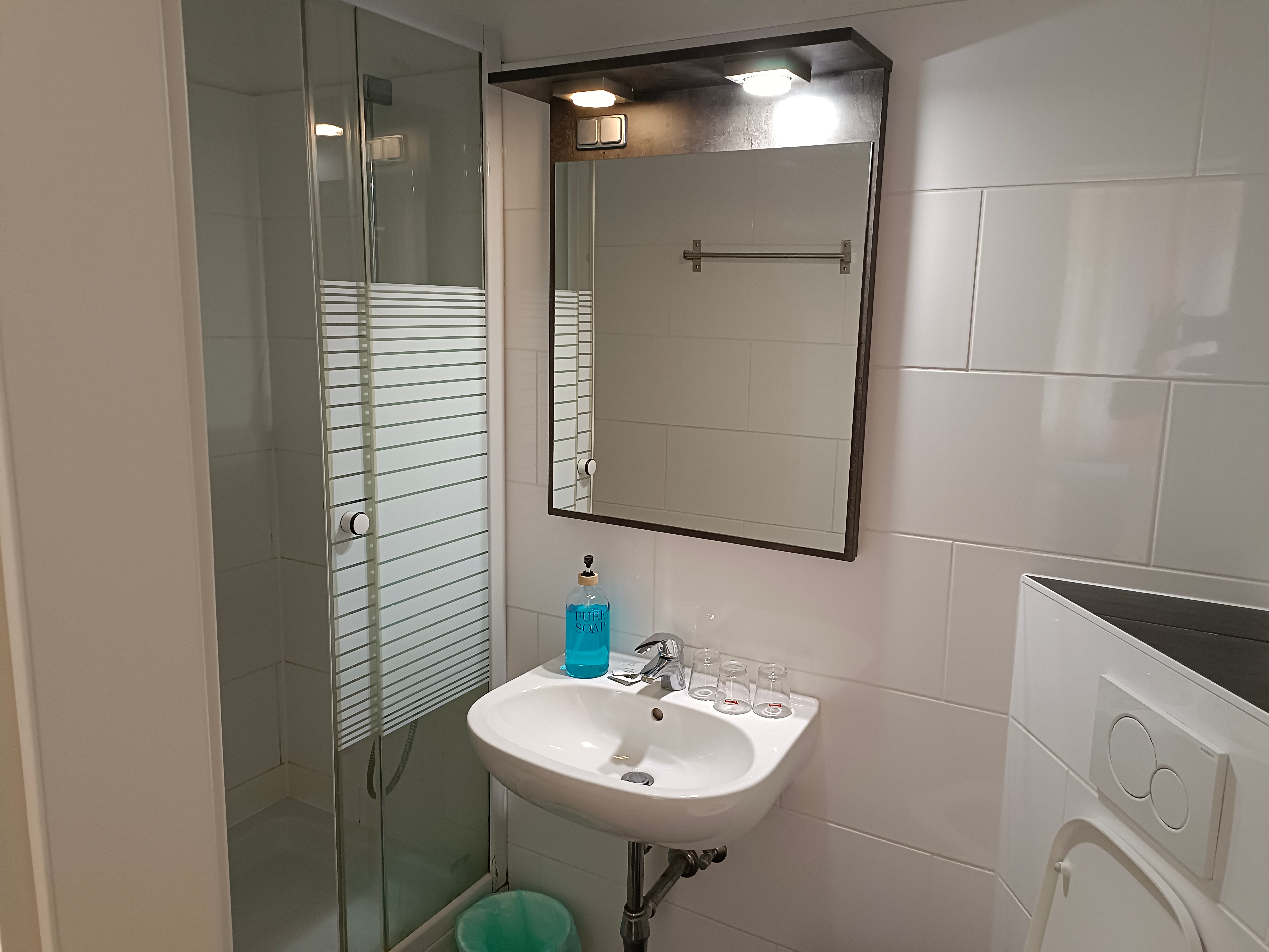 Moderná kúpeľňa so sprchovacím kútom, umývadlom a zrkadlom.
