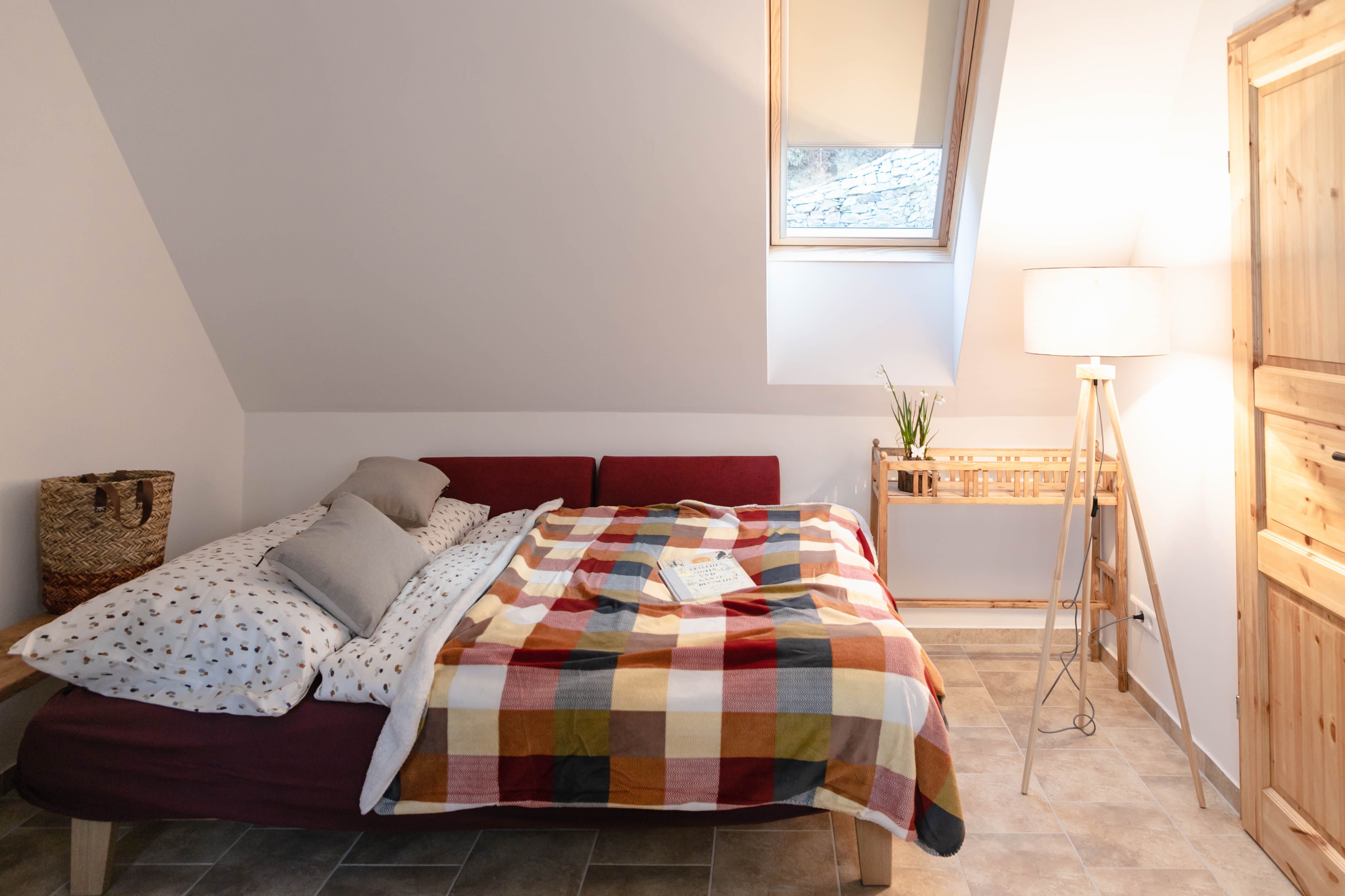 Útulná spálňa s posteľou, farebnou dekou a lampou na čítanie.