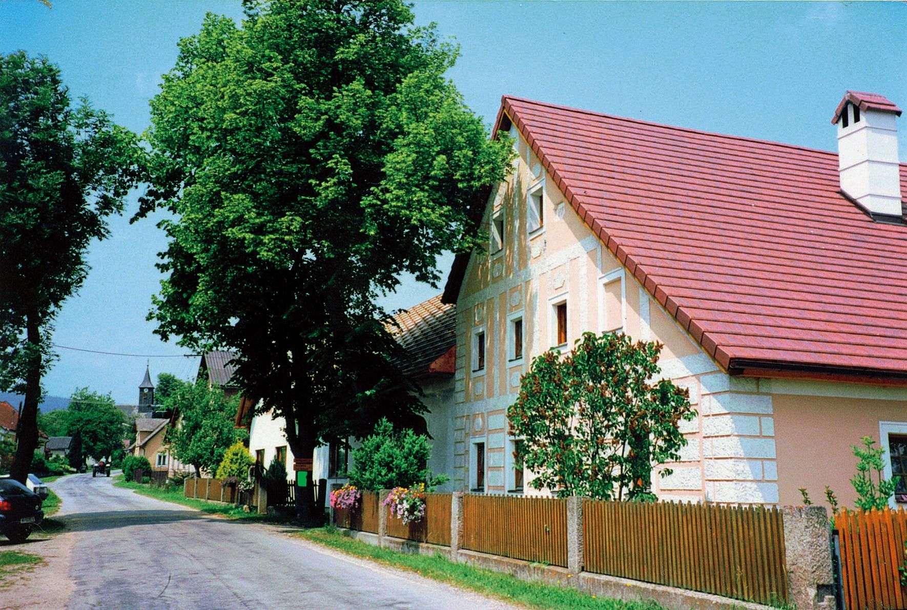 Ulica s tradičnými domami a stromami vo vidieckom prostredí.