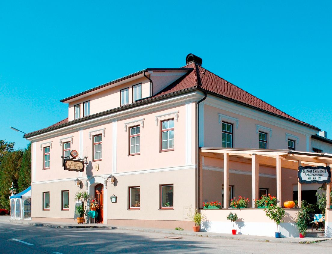 Tradičný hostinec s ružovou fasádou a červenou strechou, zdobený rastlinami a tekvicou.