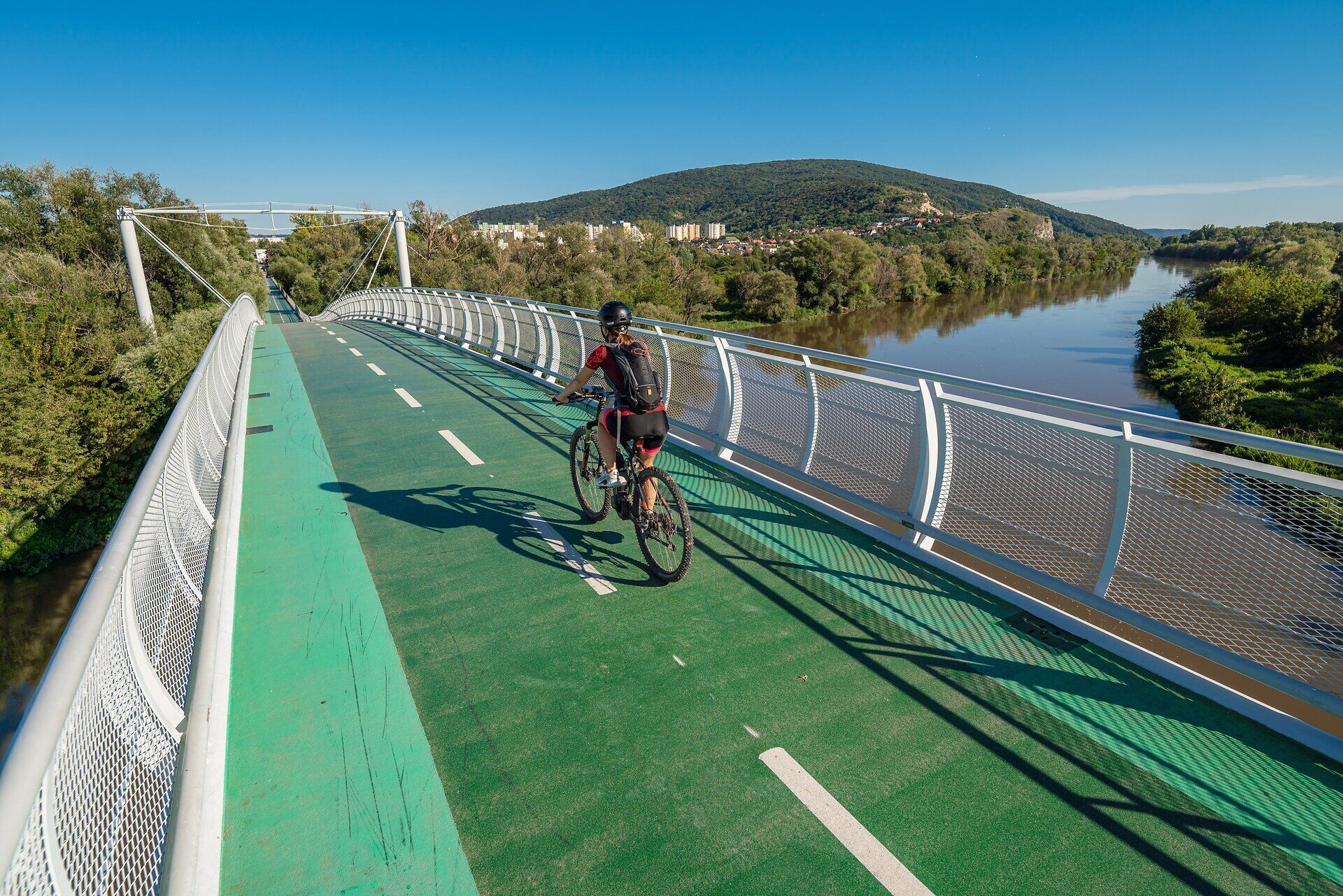 Most slobody sa majestátne tiahne cez pokojnú rieku, obklopený sviežou zeleňou a kopcami. Cyklisti si vychutnávajú čerstvý vzduch a úchvatné výhľady a zároveň zažívajú spojenie medzi prírodou a kultúrou. Ideálne miesto na nezabudnuteľný výhľad a hodiny oddychu v prírode.