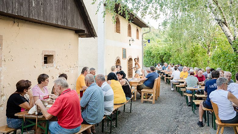 Ľudia sedia pri dlhých stoloch vonku vo Viechi.