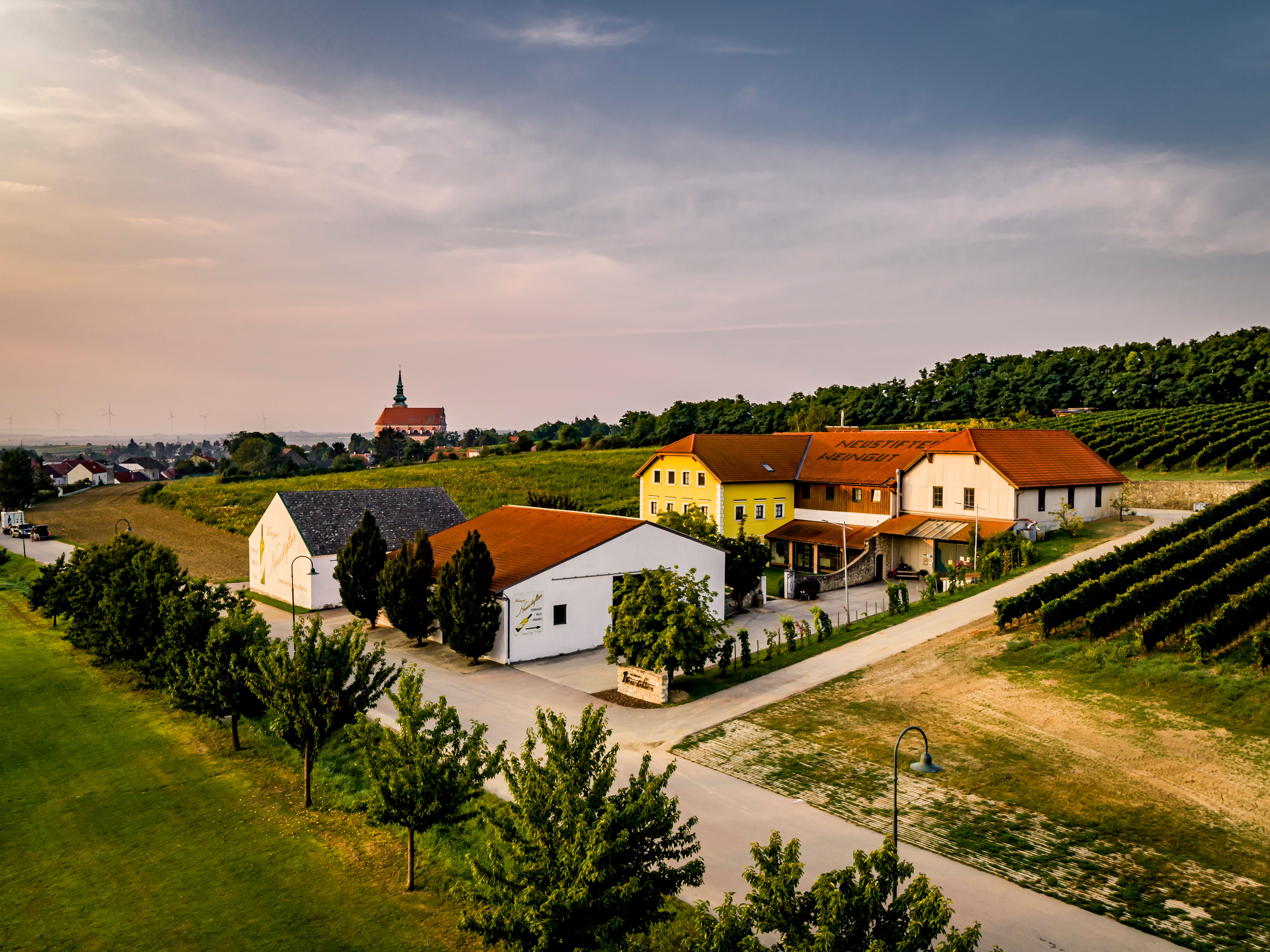 Letecký pohľad na vinárstvo s budovami a vinohradmi pri západe slnka.