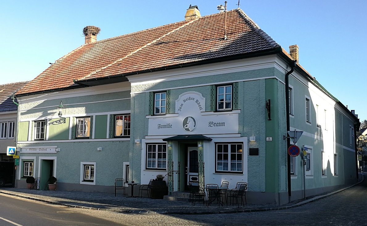 Tradičný hostinec so zelenou fasádou a názvom "Zum weißen Rössl". Pred budovou sú stoly a stoličky.