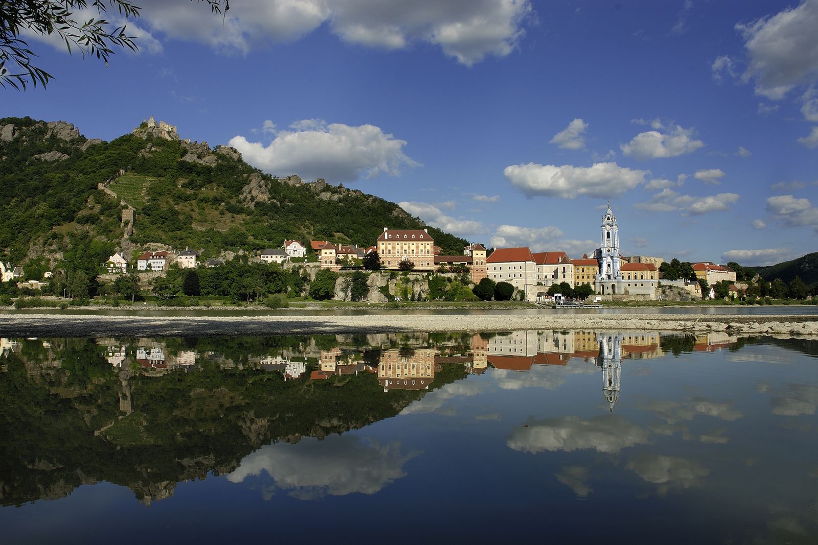 Panoráma Dürnsteinu s Dunajom v popredí a zrúcaninou hradu na kopci v pozadí.