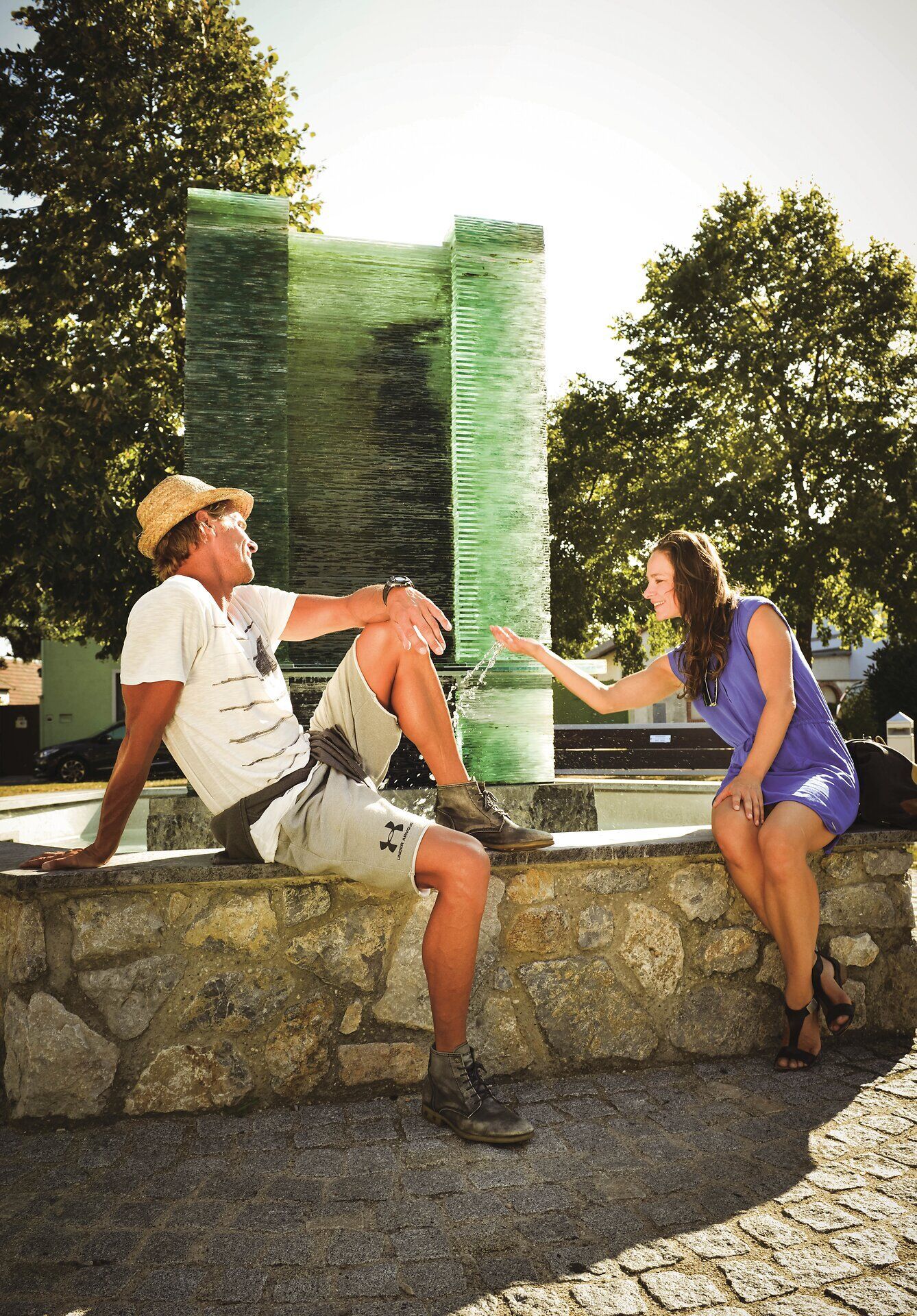 Pár sedí na stene pred fontánou. Žena sa hrá s vodou. 