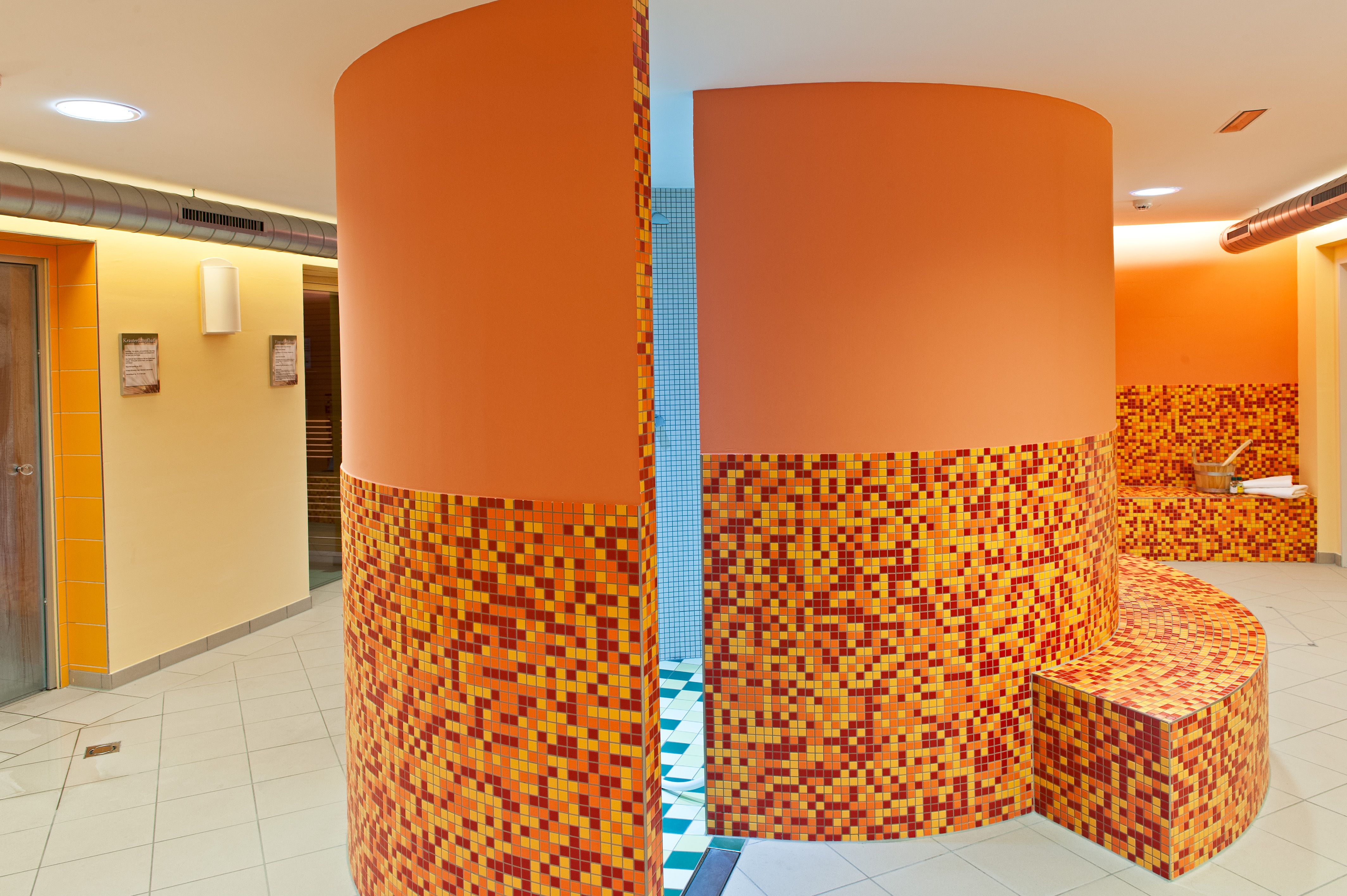 Pohľad do interiéru wellness centra s mozaikovými obkladmi oranžovej farby a oblými stenami.