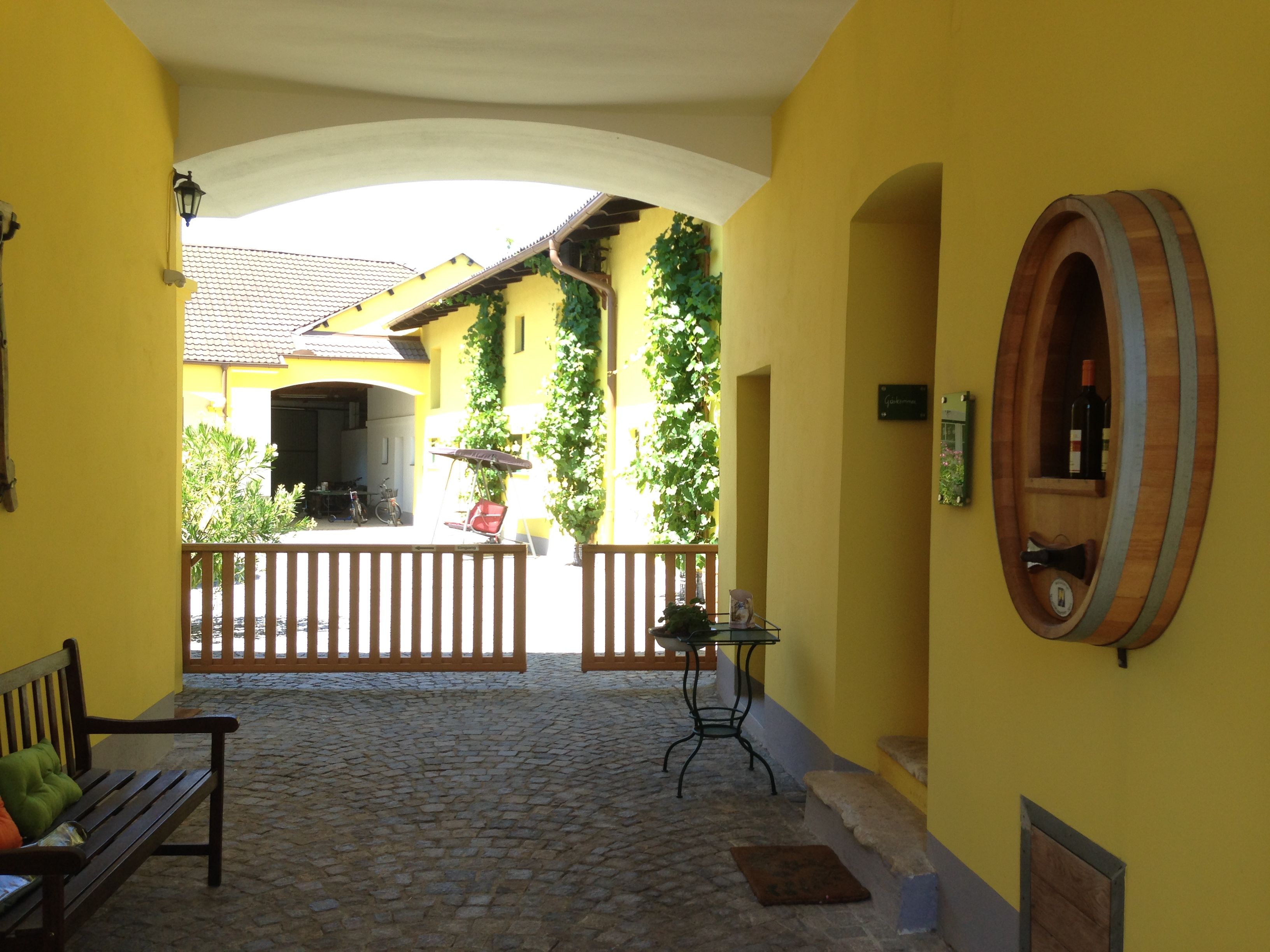Vnútorné nádvorie žltej budovy s výzdobou sudov na víno a drevenou bránou.