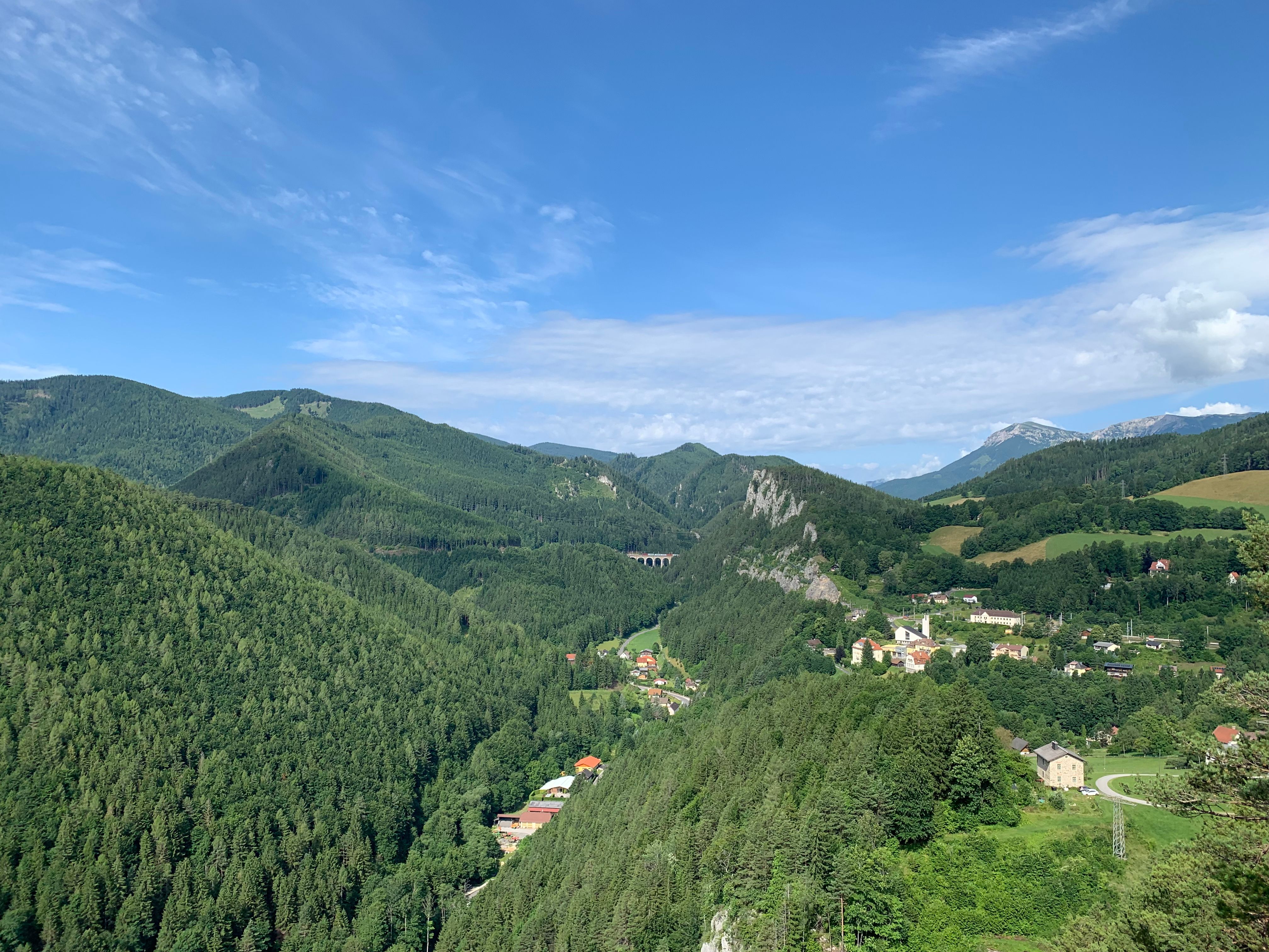 Panoramatický pohľad na zelenú horskú krajinu s malou dedinou a viaduktom.
