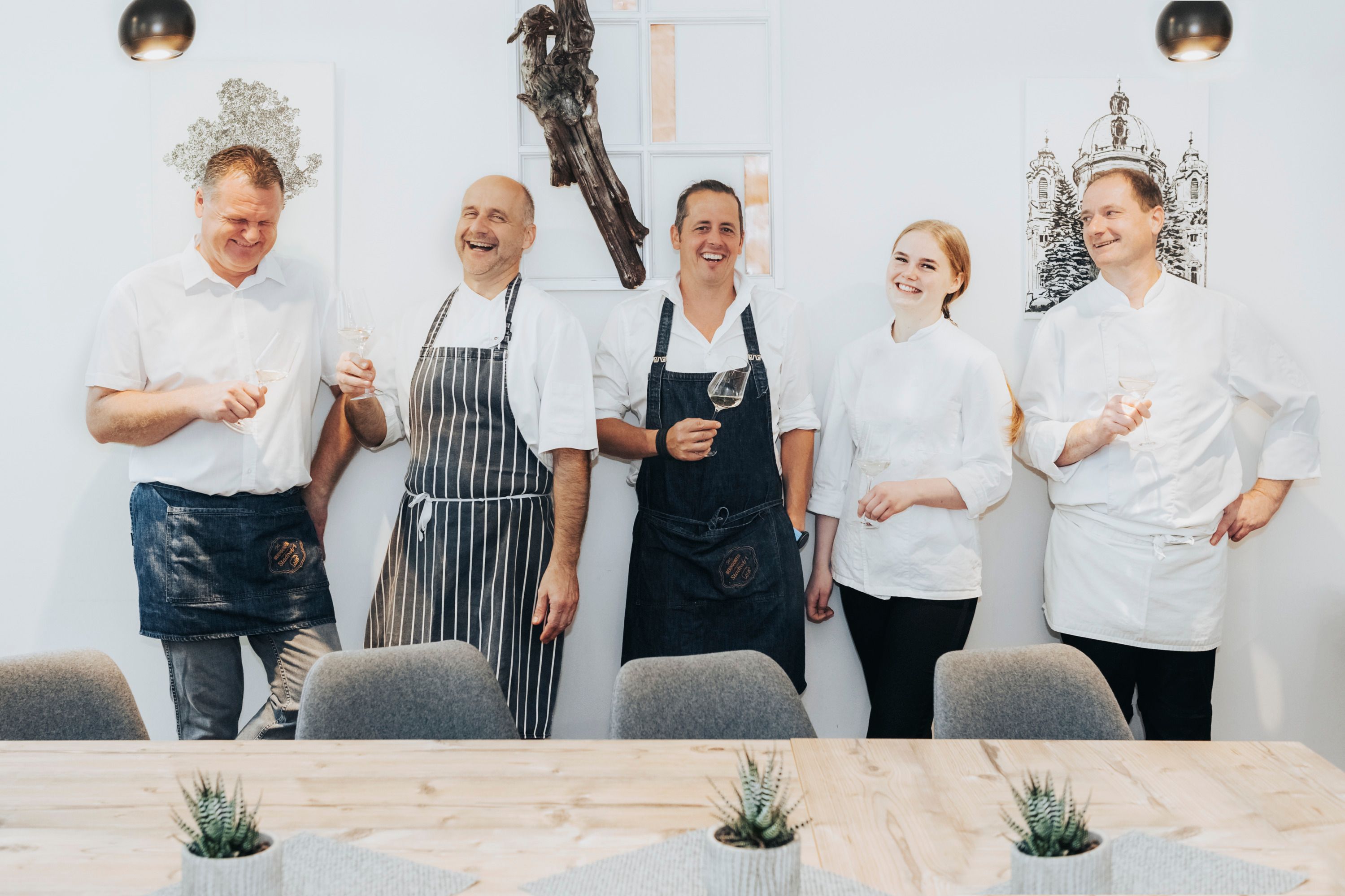 Päť ľudí oblečených ako kuchári sa smeje a drží poháre s vínom.