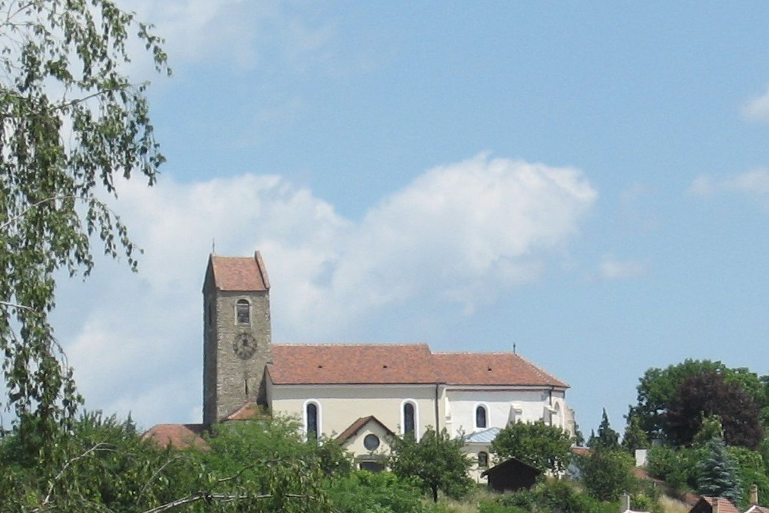 Kostol s vežou a červenou strechou v Hohenwarte, obklopený stromami a modrou oblohou.