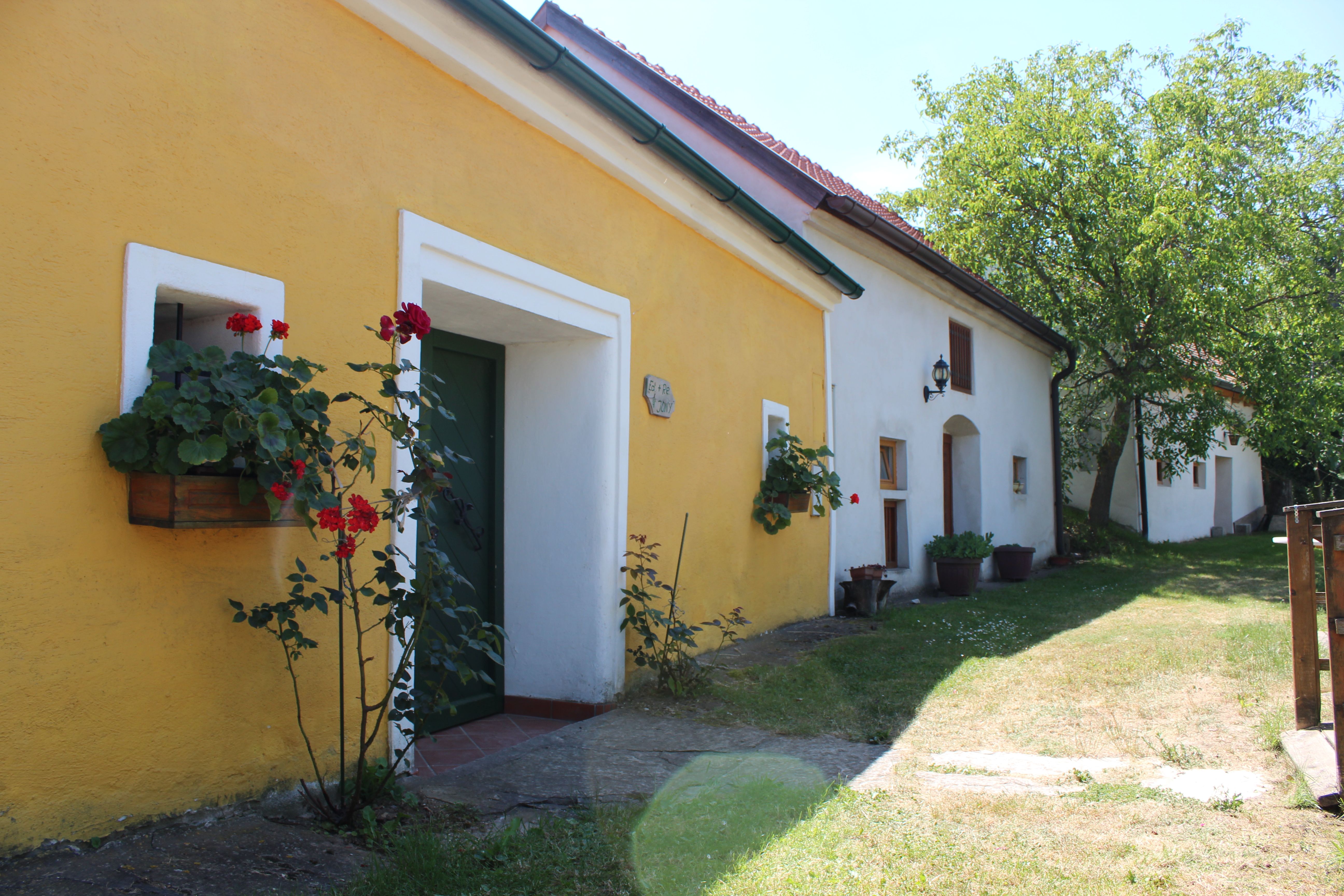 Žlto-biela budova v Vínnejch uličkách s kvetmi a stromami.