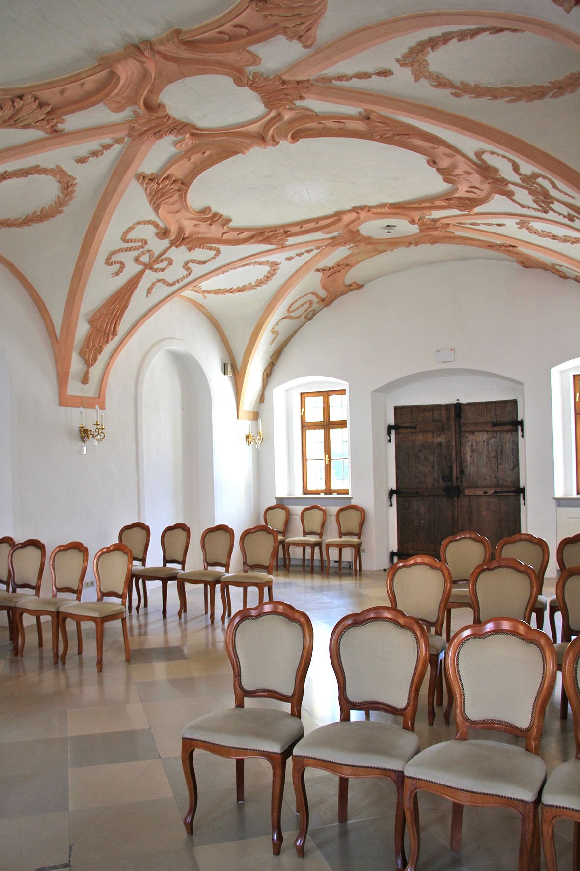 Pohľad do interiéru historickej miestnosti so zdobenými štukovými stropmi a elegantnými drevenými stoličkami.