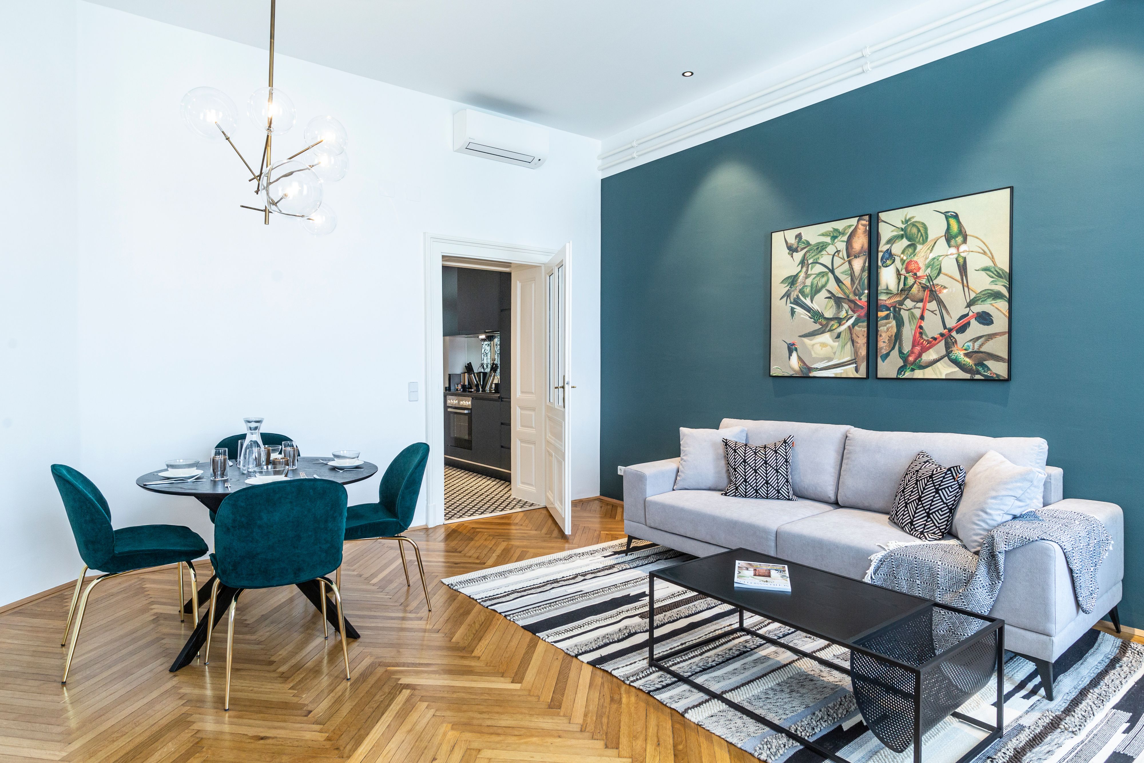 Moderná obývacia izba so sivou pohovkou, jedálenským stolom a umeleckými dielami na stene.