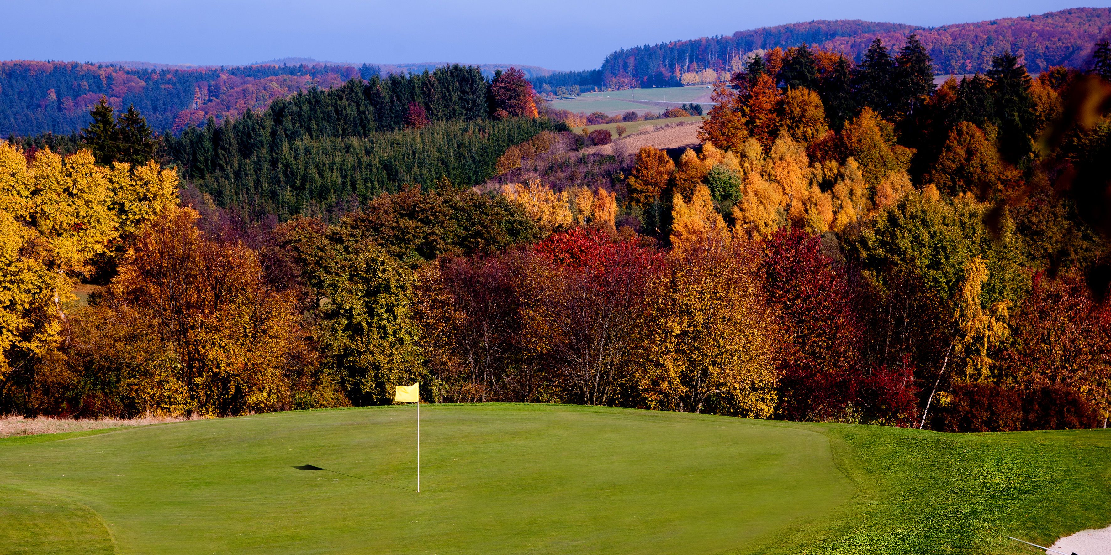 Golfové ihrisko s jesennými stromami v pozadí, žltá vlajka na greene.