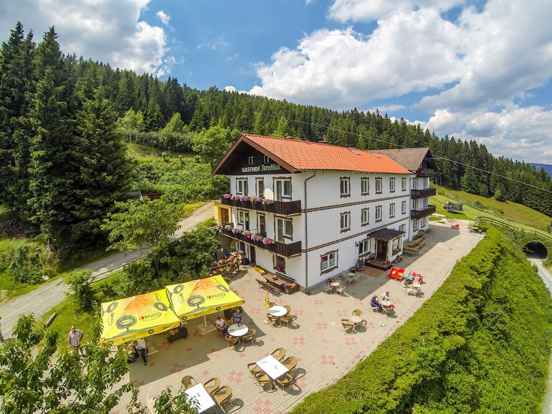 Alpský hostinec s terasou a slnečníkmi v horskej krajine.