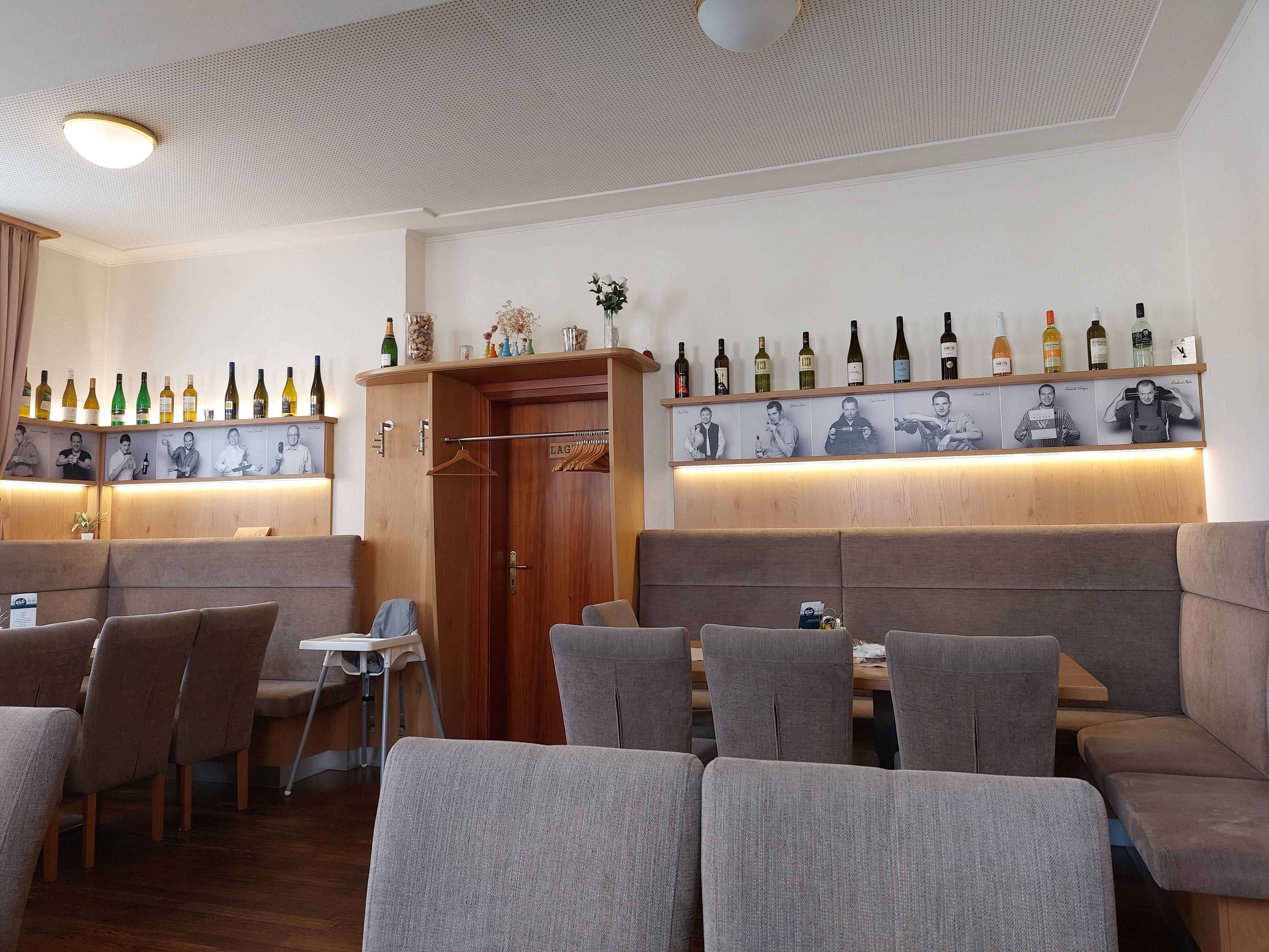 Pohľad do interiéru reštaurácie s fľašami vína a čiernobielymi fotografiami na stene.