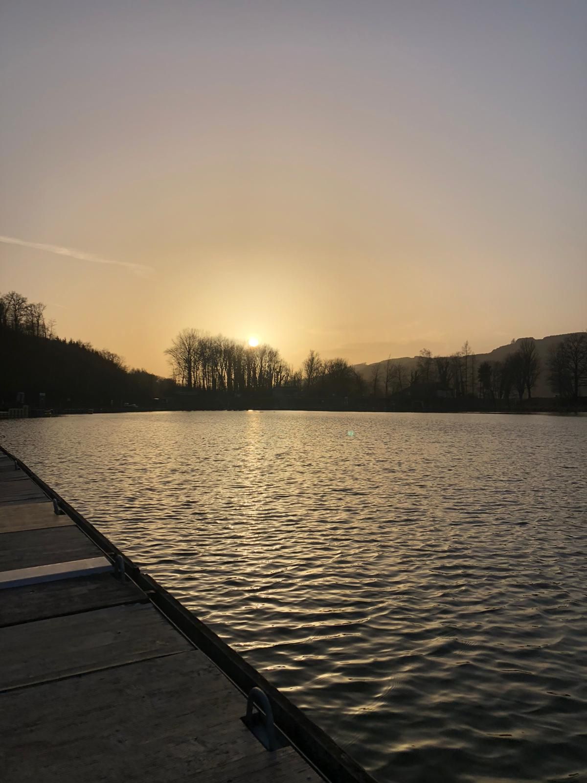 Západ slnka nad prístavom s mólom a stromami v pozadí.