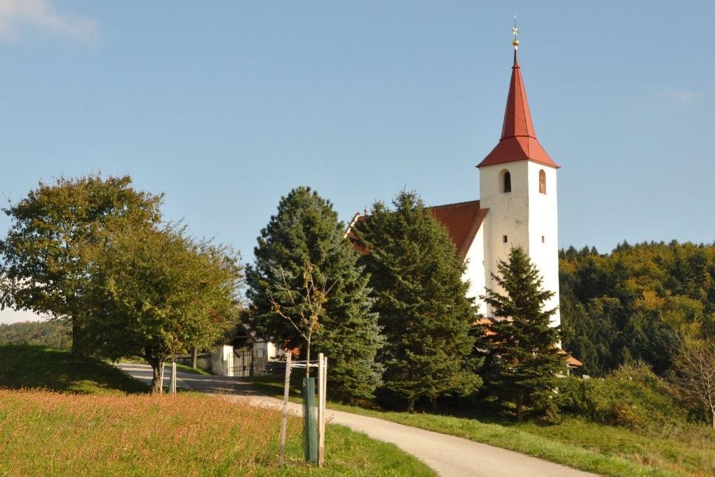Farský kostol v Ofenbachu s červenou strechou veže, obklopený stromami a lúkami.