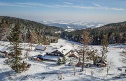 Lyžiarsky areál so sedačkovou lanovkou a lyžiarmi, obklopený zasneženými stromami a kopcami.
